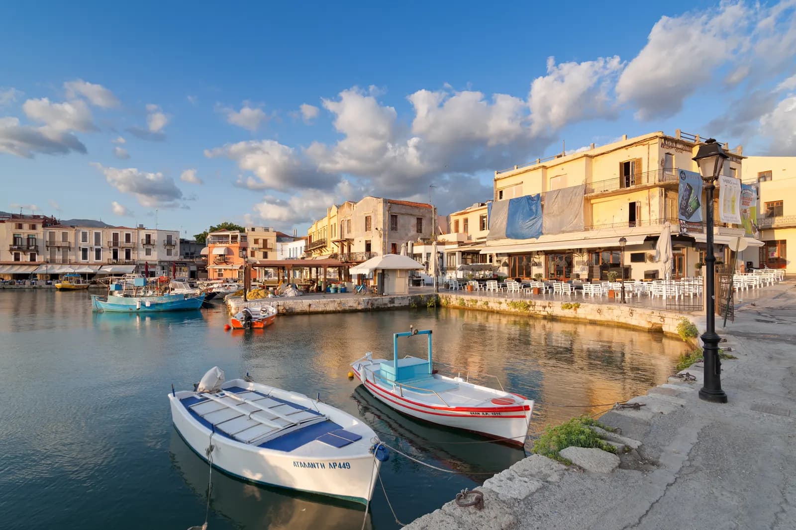 Small fishing boats moored in the Venetian harbour of Rethymno in front of waterfront restaurants in early morning light