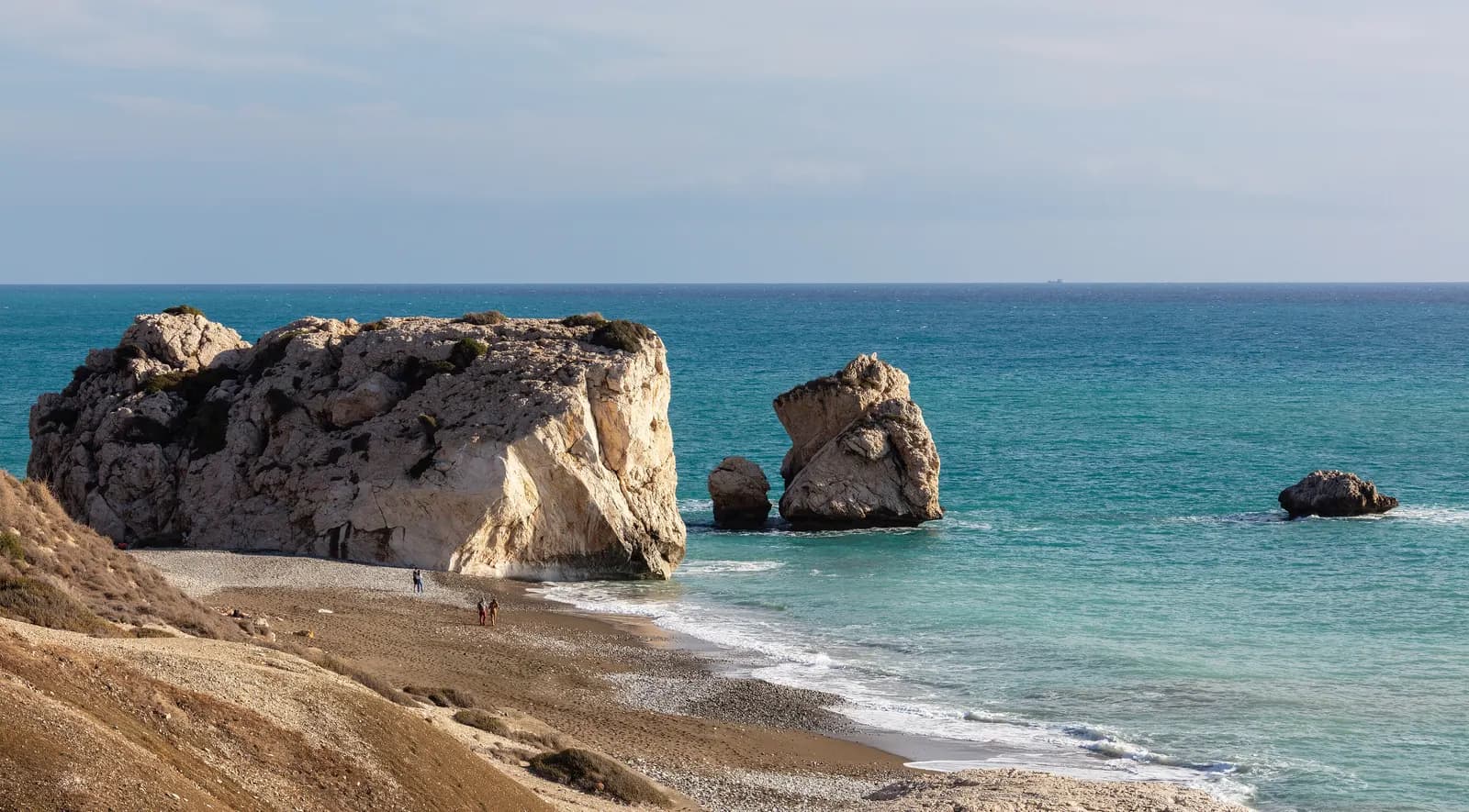 The rocks of Petra tou Romiou, known as Aphrodite's Rock, rising from turquoise water beside a pebble beach on the coast of Paphos District, seen from the hillside above