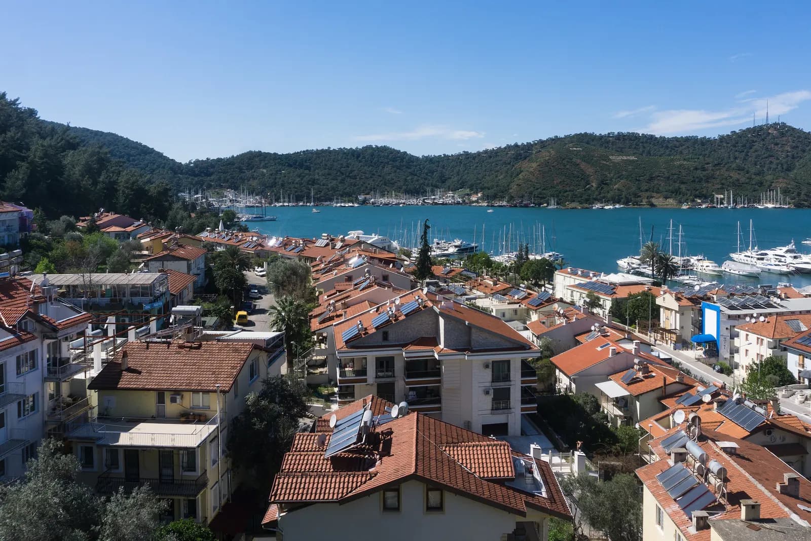 Tiled roofs of Fethiye town above the harbour, with yachts moored in the marina and wooded hills across the bay