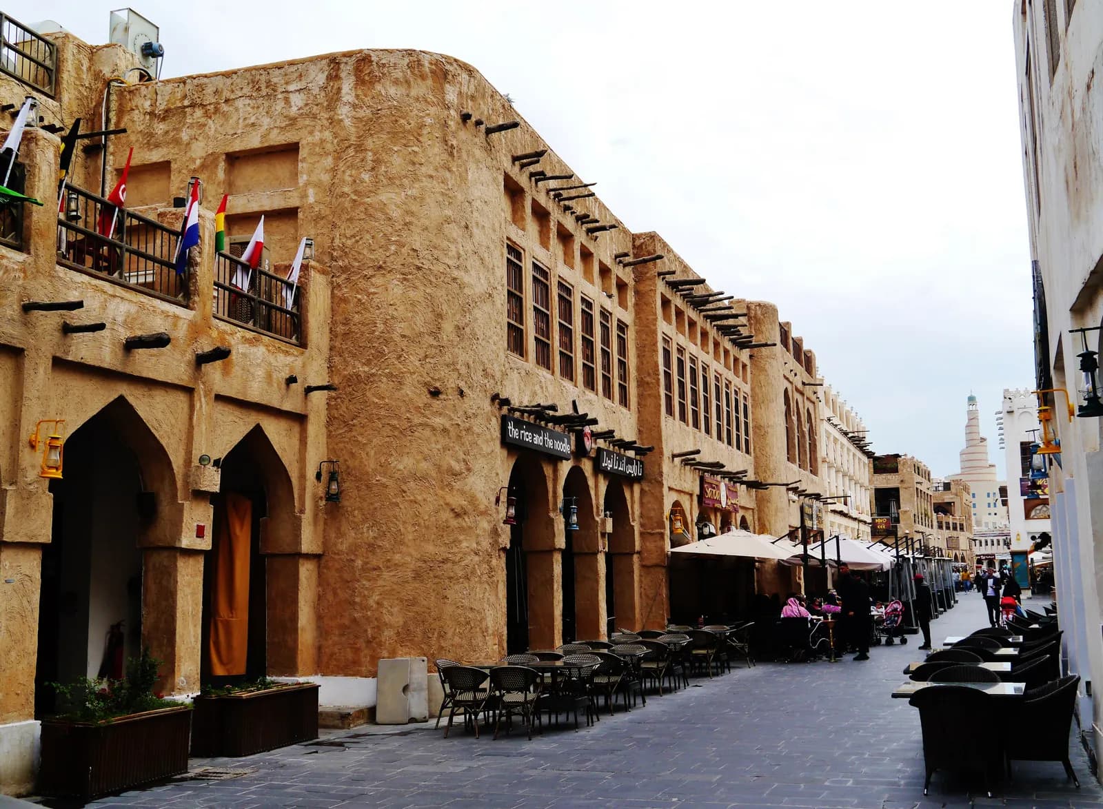 The main street of Souq Waqif, with mud-rendered buildings, wooden roof beams, lanterns and café tables along a paved lane