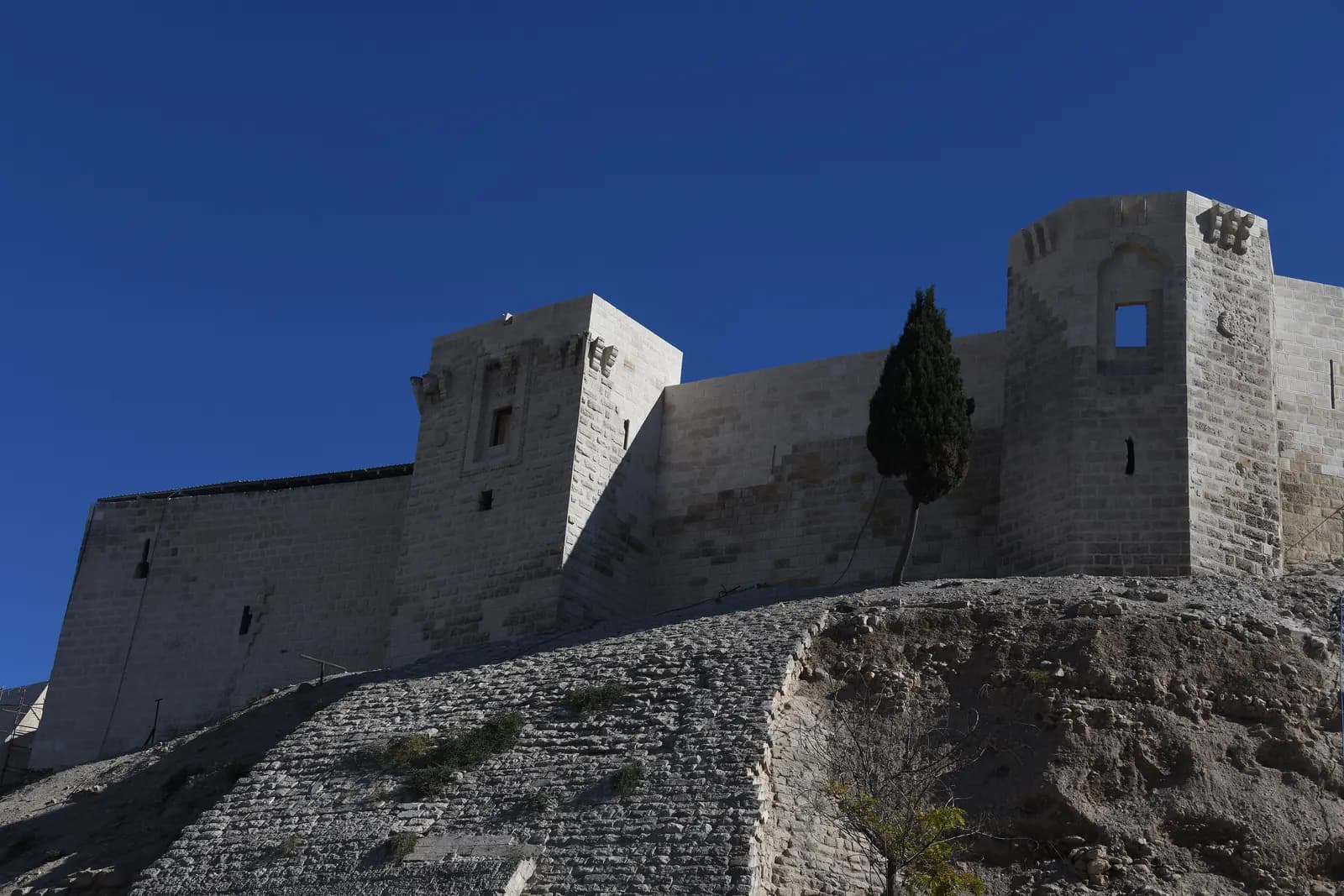 The stone walls and towers of Gaziantep Castle above its paved mound under a deep blue sky