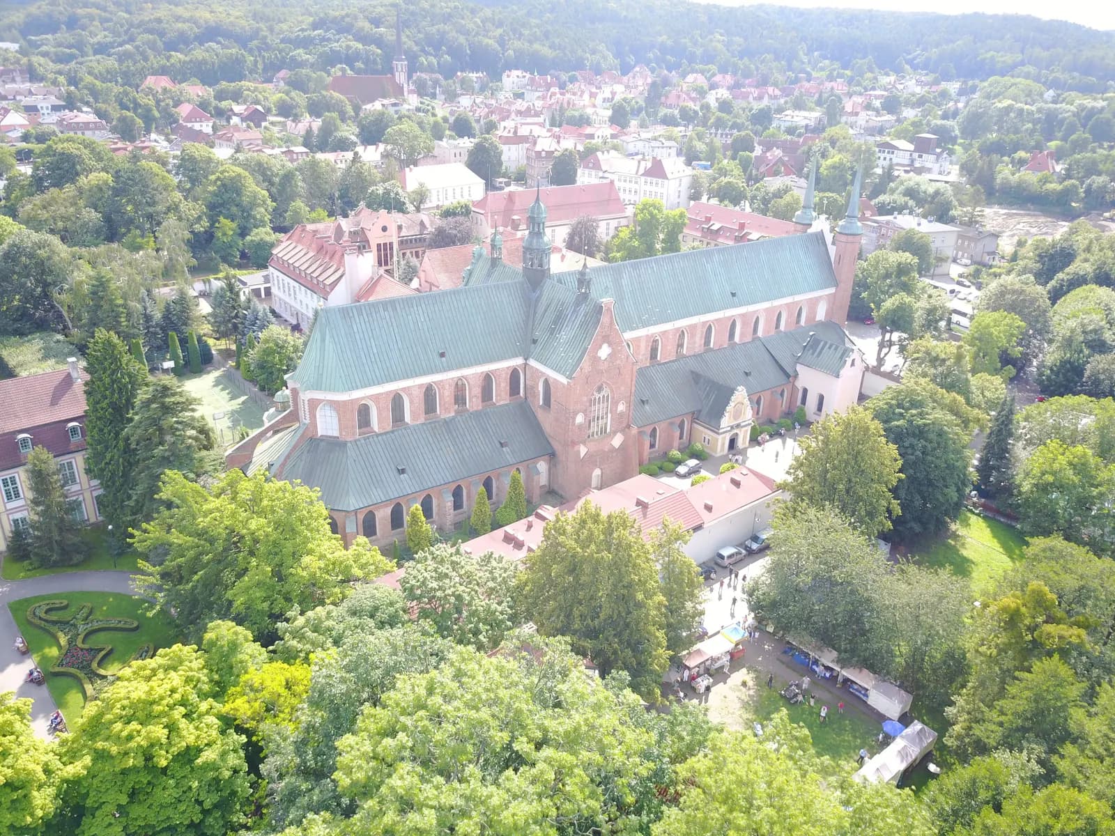Aerial view of Oliwa Cathedral in Gdańsk with its green copper roofs and twin towers, surrounded by the trees of Oliwa Park and the houses of the district