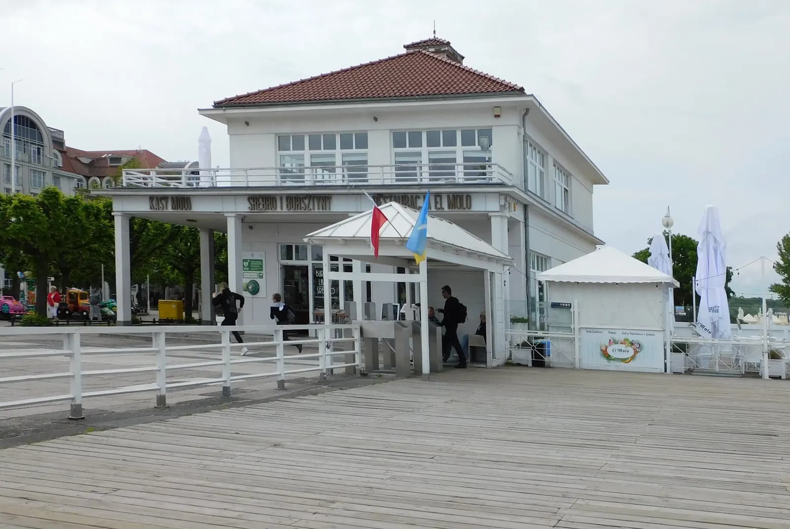 A white two-storey pavilion with a red roof on the wooden deck of Sopot pier, with flags at the entrance