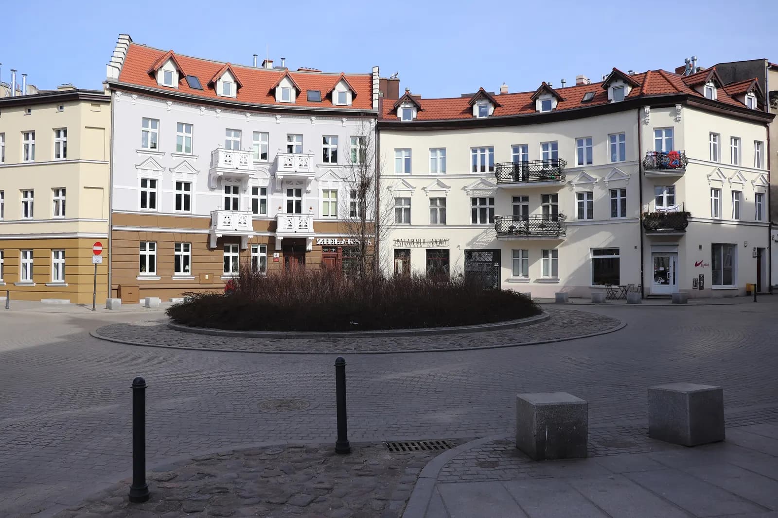 Restored white tenements with red tiled roofs and balconies around a round planted island on Wajdeloty Street in Gdańsk Wrzeszcz