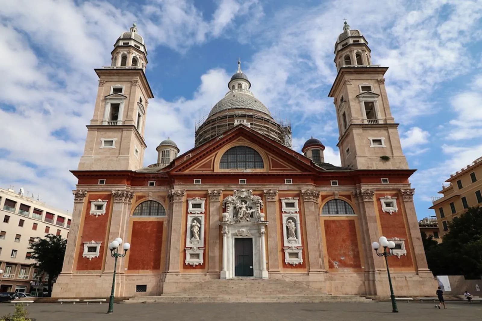The twin-towered basilica of Santa Maria Assunta di Carignano in Genoa, its dome under scaffolding, above a broad empty terrace.