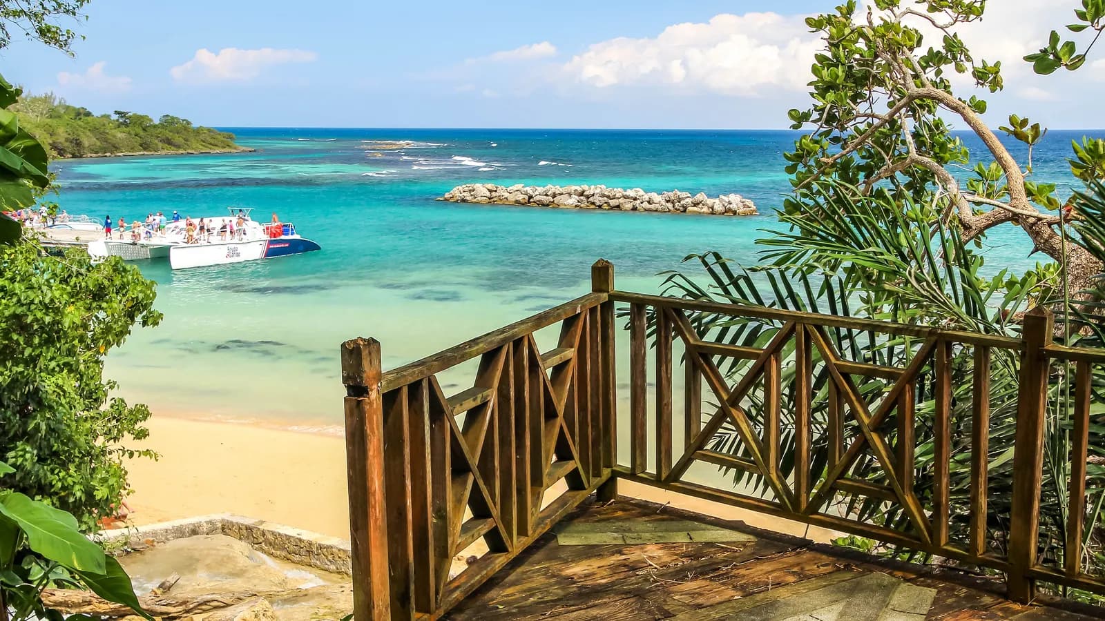 The beach at Dunn's River Falls near Ocho Rios seen from a wooden lookout, with turquoise water, a breakwater and catamarans at a jetty