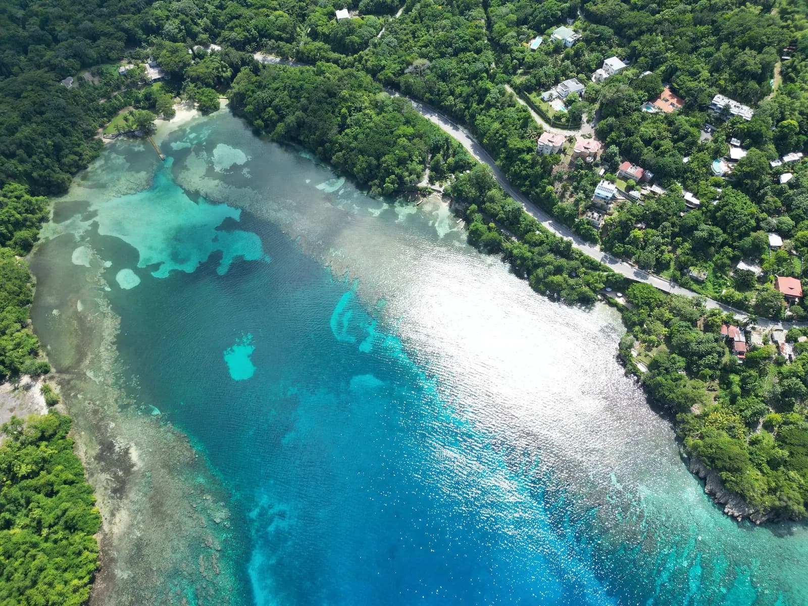Aerial view of the bay at San San, Port Antonio, with a reef in turquoise water, a coast road and houses among thick forest