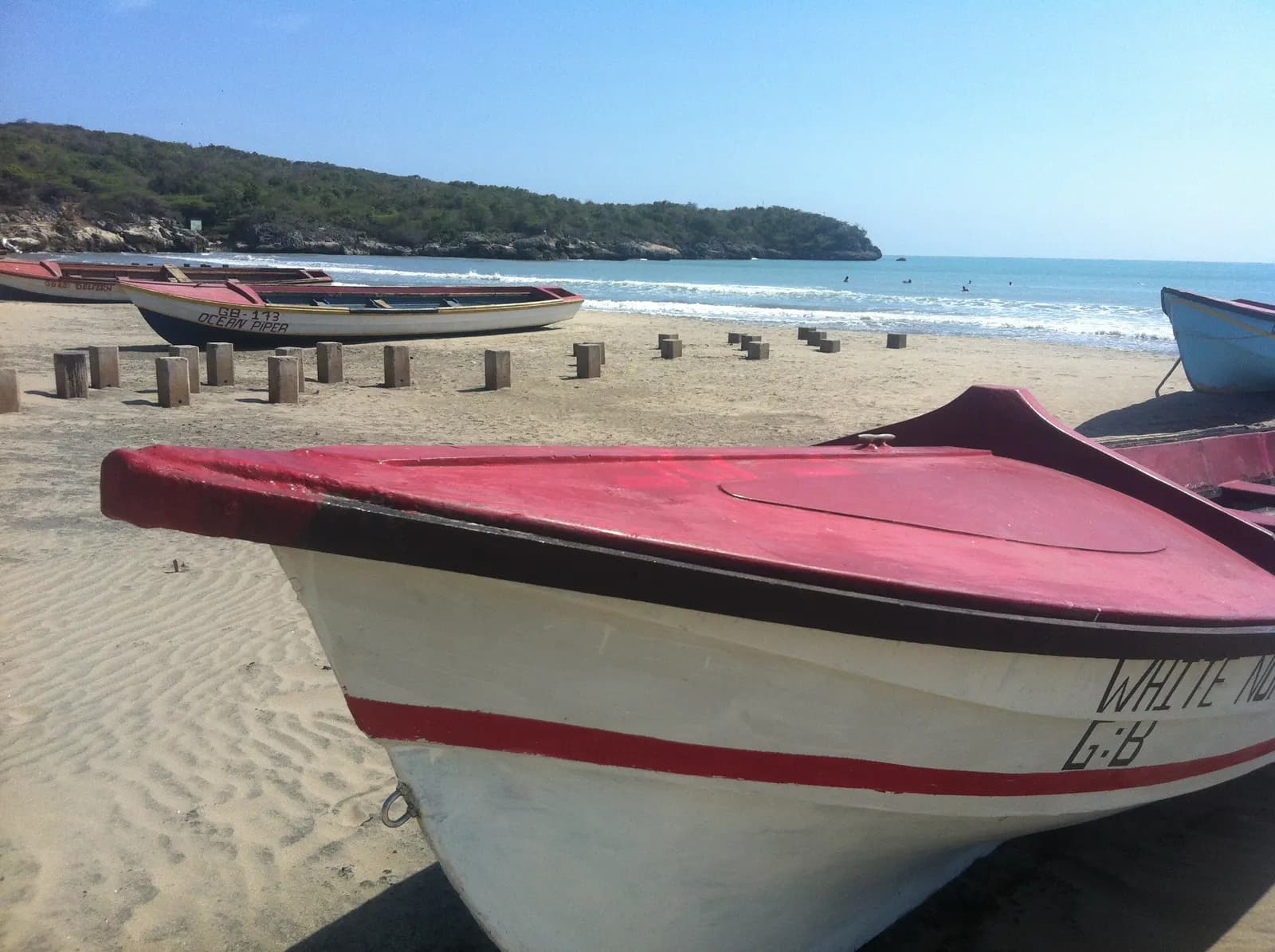 Wooden fishing boats pulled up on the sand at Great Bay Beach, Treasure Beach, with a green headland across the water