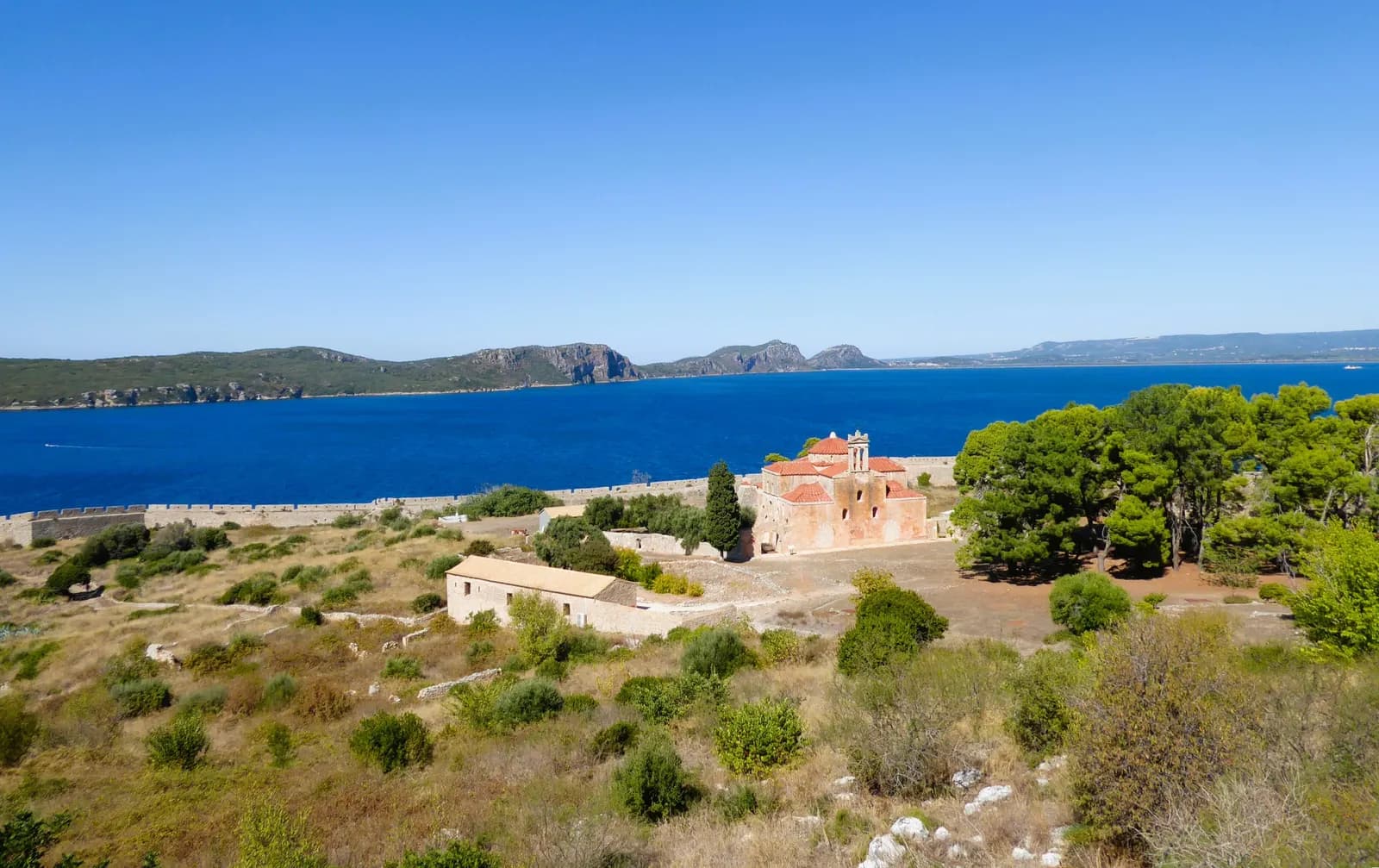 Navarino Bay seen from the Neokastro fortress at Pylos, with an old church and pines inside the walls, the deep blue bay and the hills across it