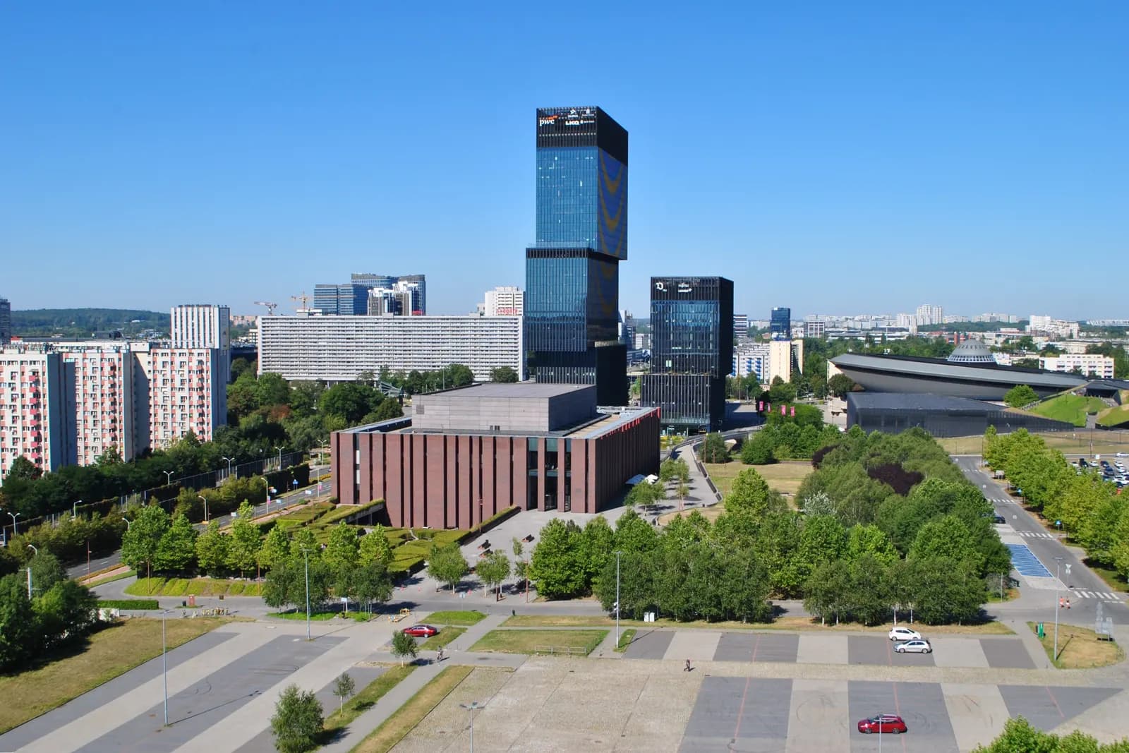 The Katowice Culture Zone from above: the red-brick concert hall of the Polish National Radio Symphony Orchestra among trees, office towers behind and the Spodek arena on the right