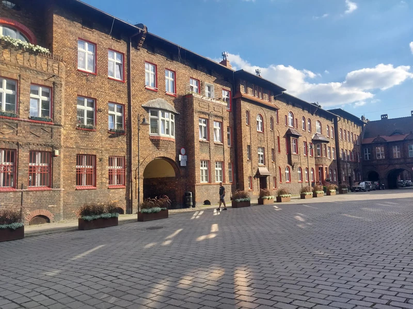 Red-brick houses with red window frames and an arched gateway around a cobbled square in Nikiszowiec, Katowice