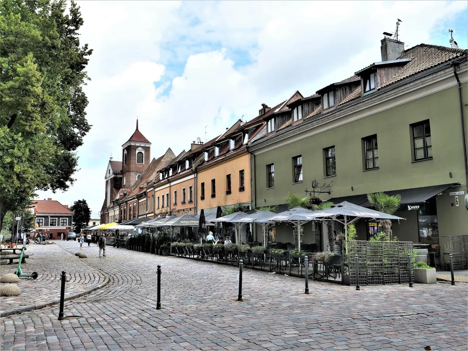 Café terraces along a cobbled street in Kaunas Old Town, with the brick tower of the cathedral of St Peter and St Paul at the end