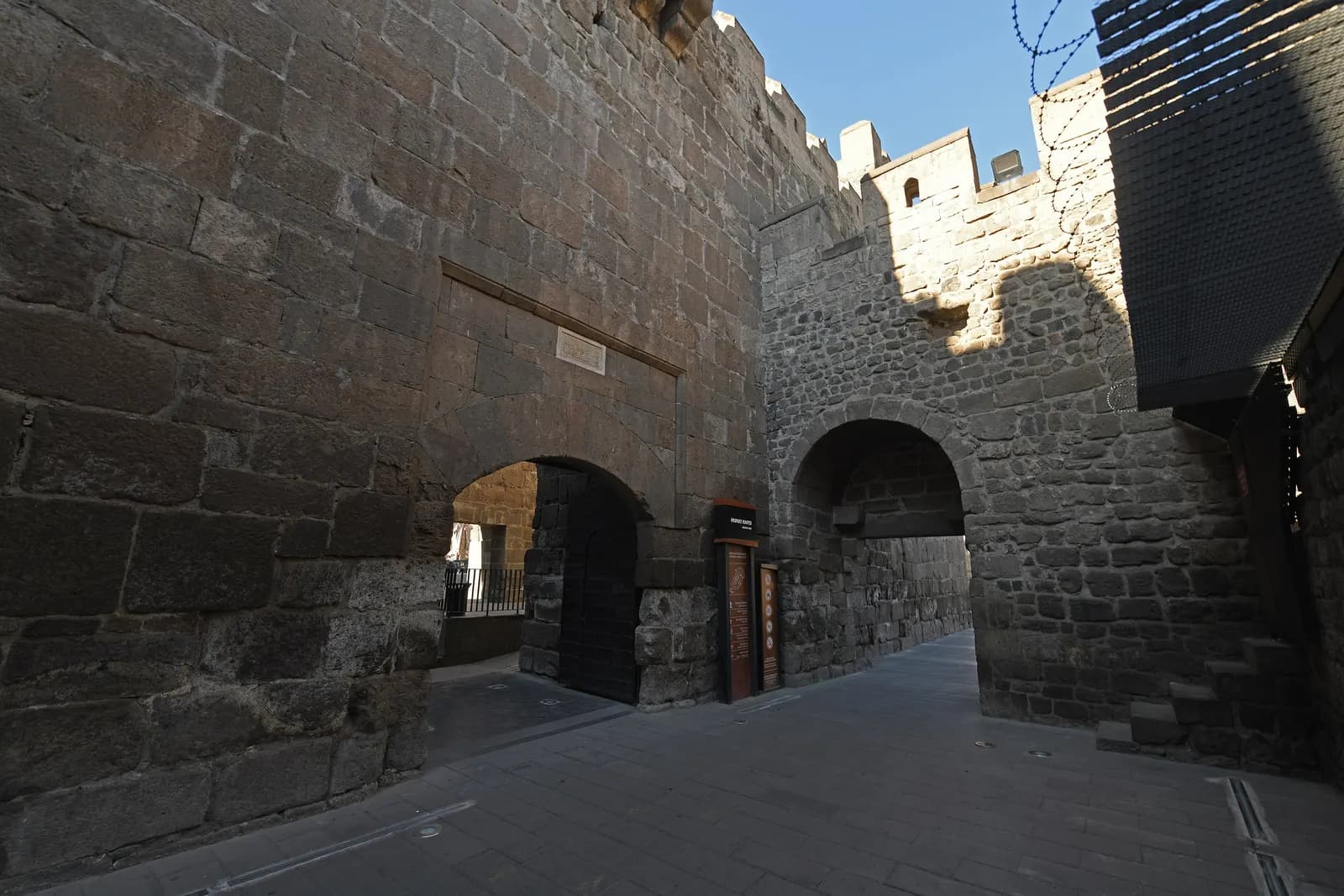 Dark basalt walls and two arched gateways of Kayseri Castle on its east side, with a paved lane between them
