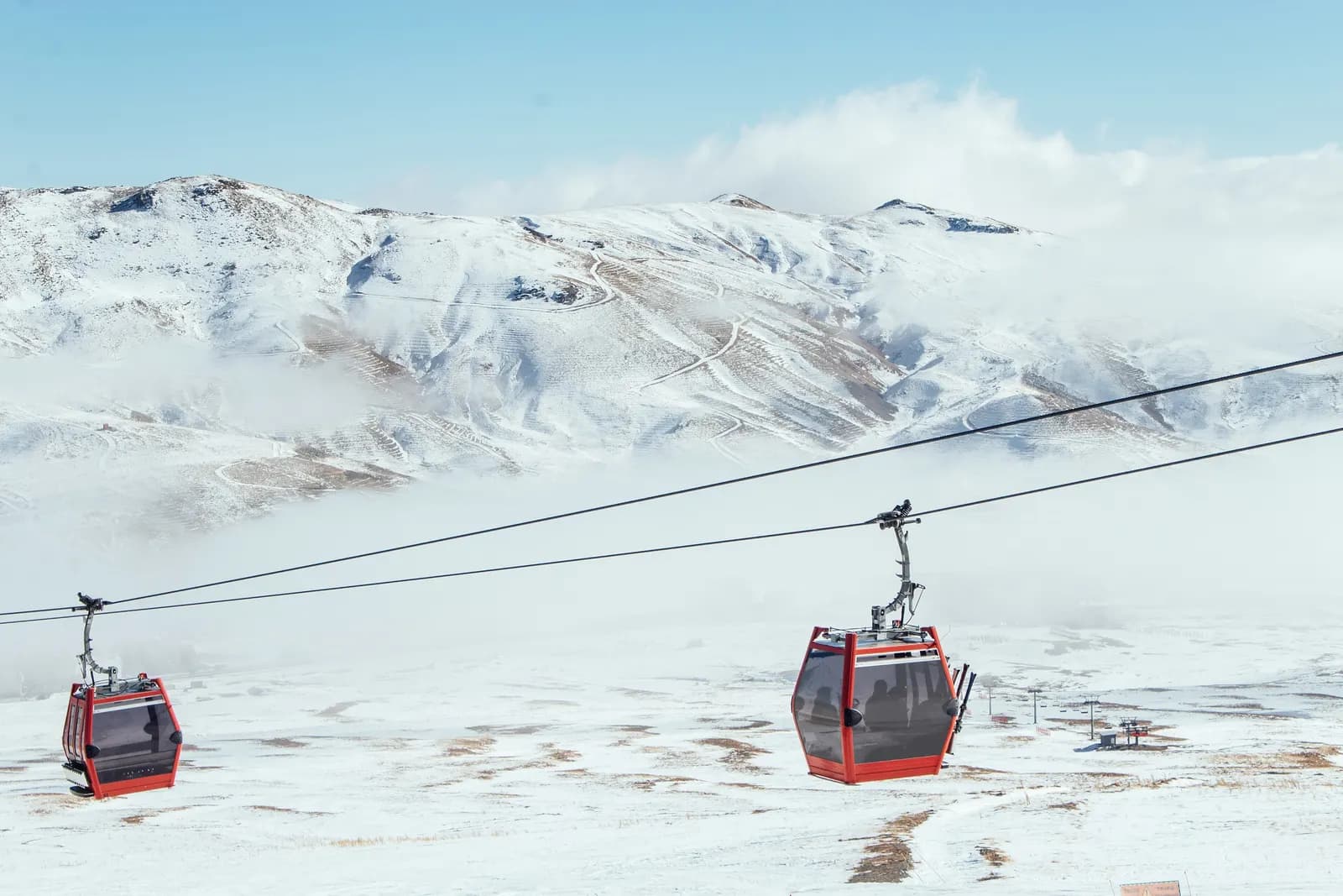Two red gondola cabins on a cable above snowy slopes at the Erciyes ski resort, with low cloud over the mountains