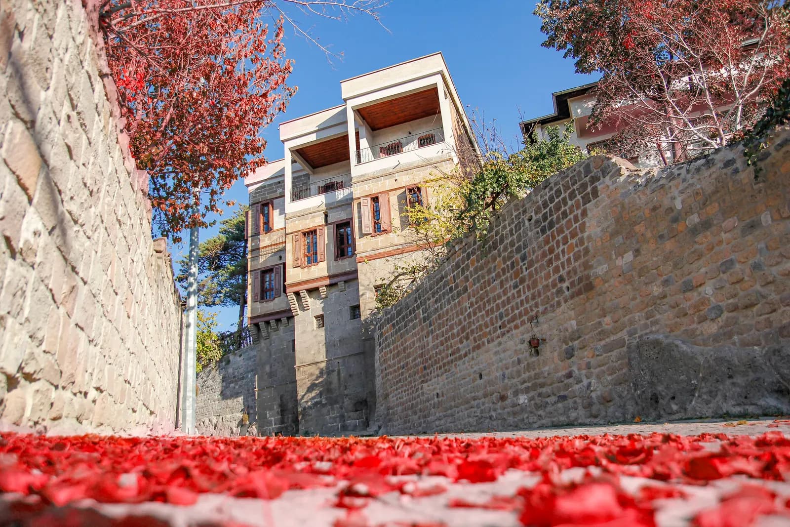 The Yaman Dede mansion in Talas, a stone house with wooden balconies above a walled lane covered in red autumn leaves