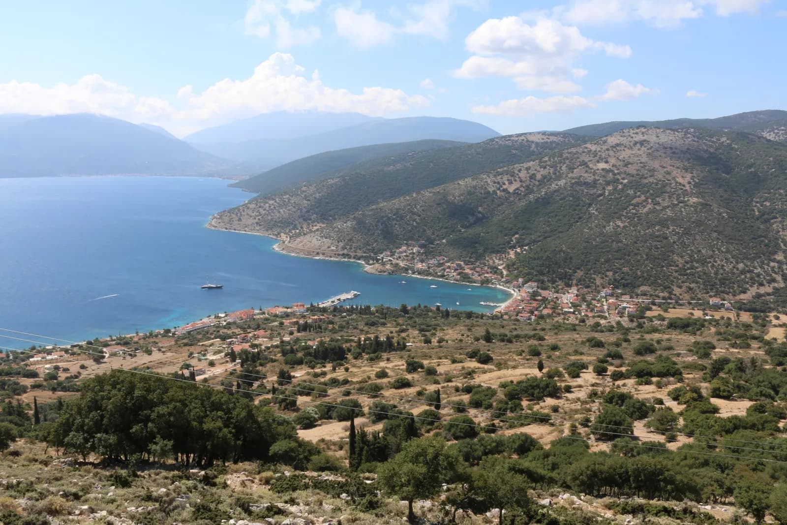 Agia Efimia seen from the hillside above, a village of red roofs curving around a bay with a small harbour, wooded hills and mountains behind