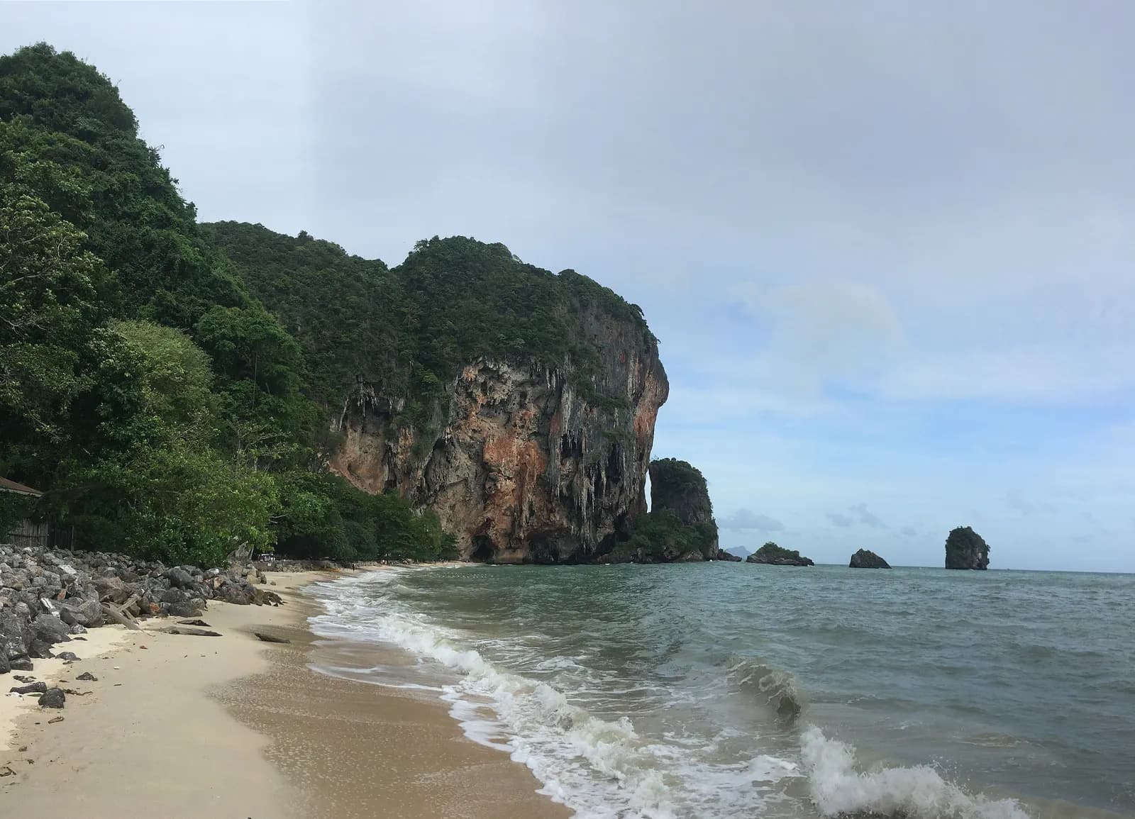 Phra Nang Beach at the south of the Railay peninsula, with waves on the sand below a tall limestone cliff and rock islets offshore