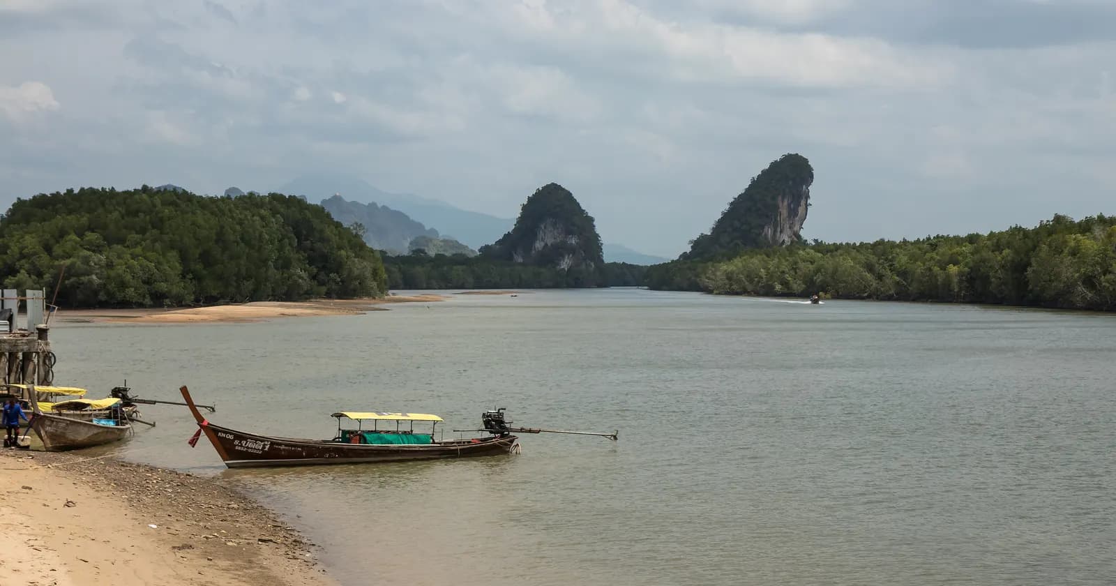 The Krabi River at Krabi town, with longtail boats on the shore, wooded banks and the twin limestone peaks of Khao Khanab Nam