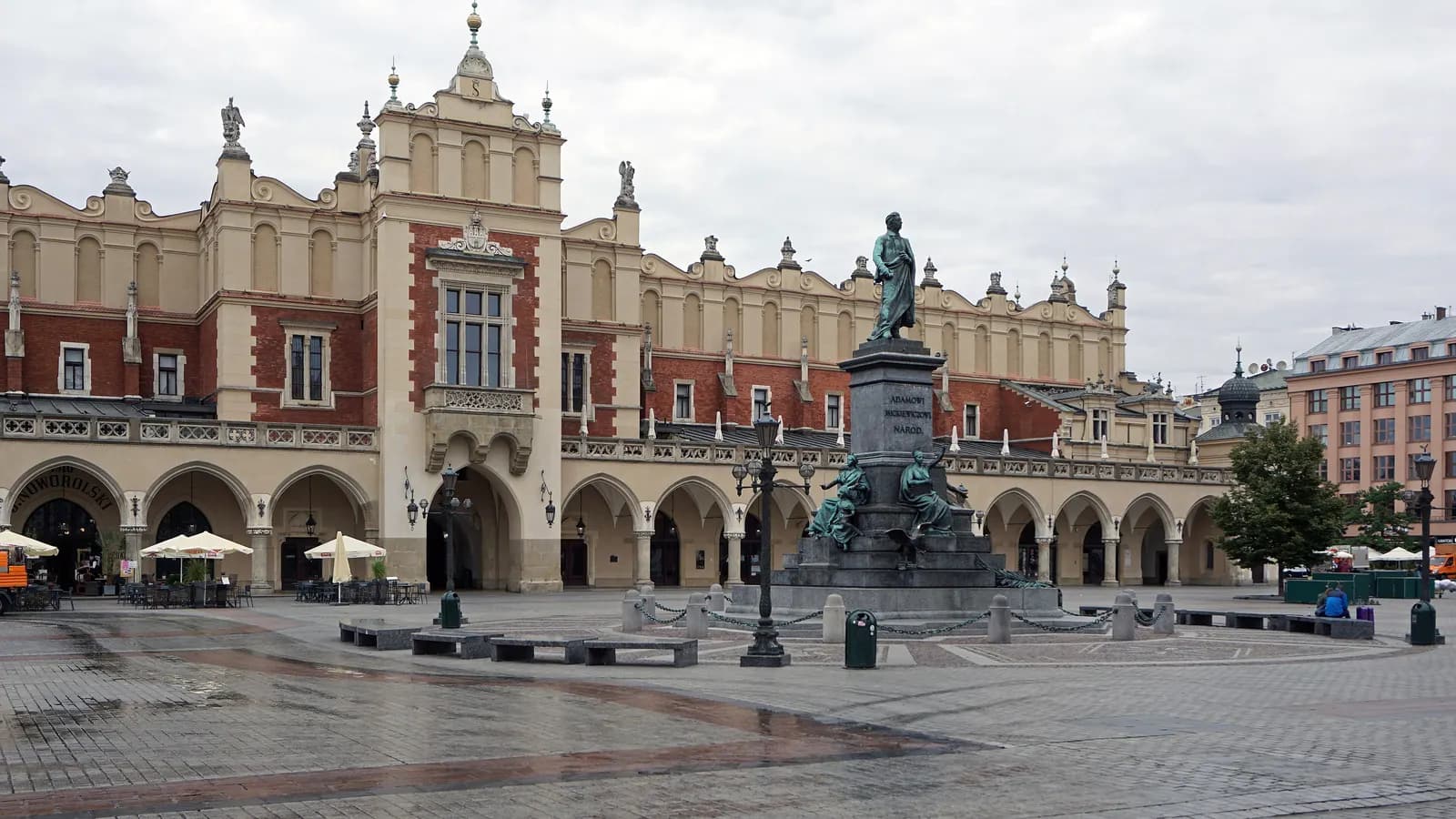 The Cloth Hall and the Adam Mickiewicz monument on Kraków's Main Market Square, with café umbrellas along the arcades