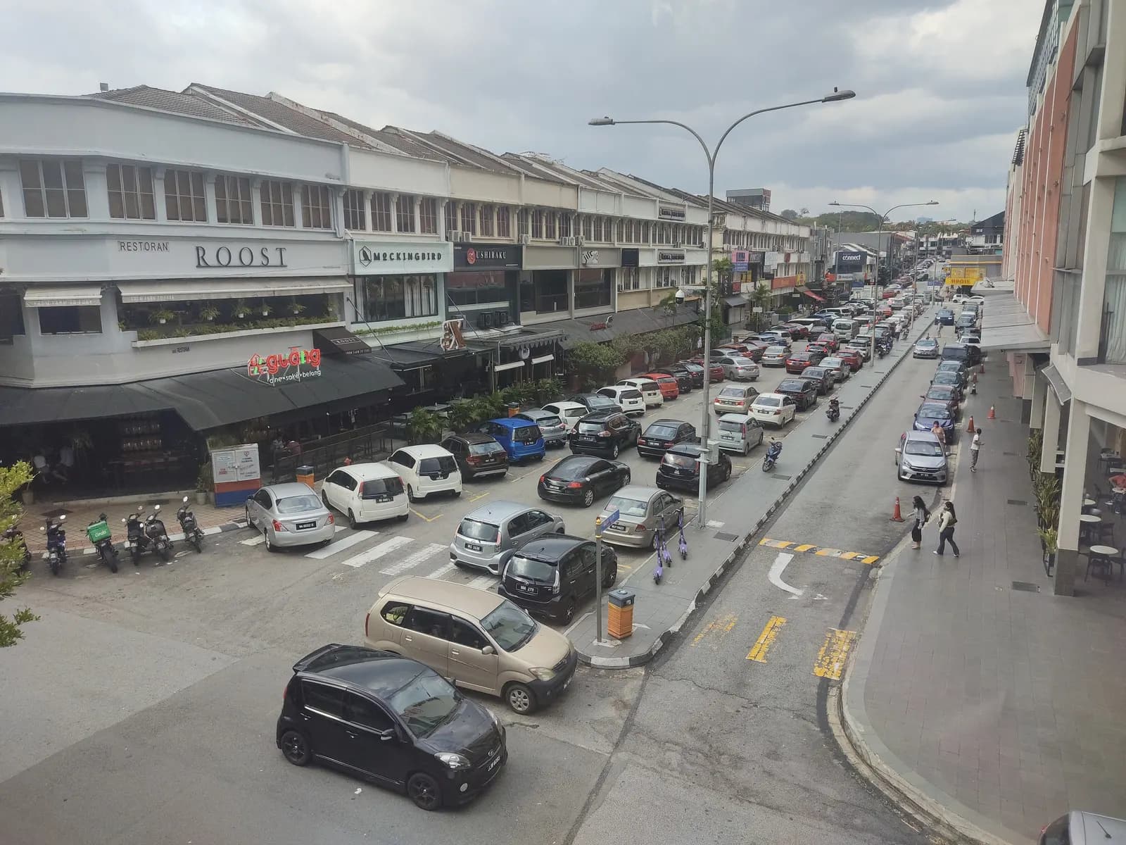 Rows of parked cars in front of the shophouse restaurants of Bangsar Baru, seen from above on a cloudy afternoon