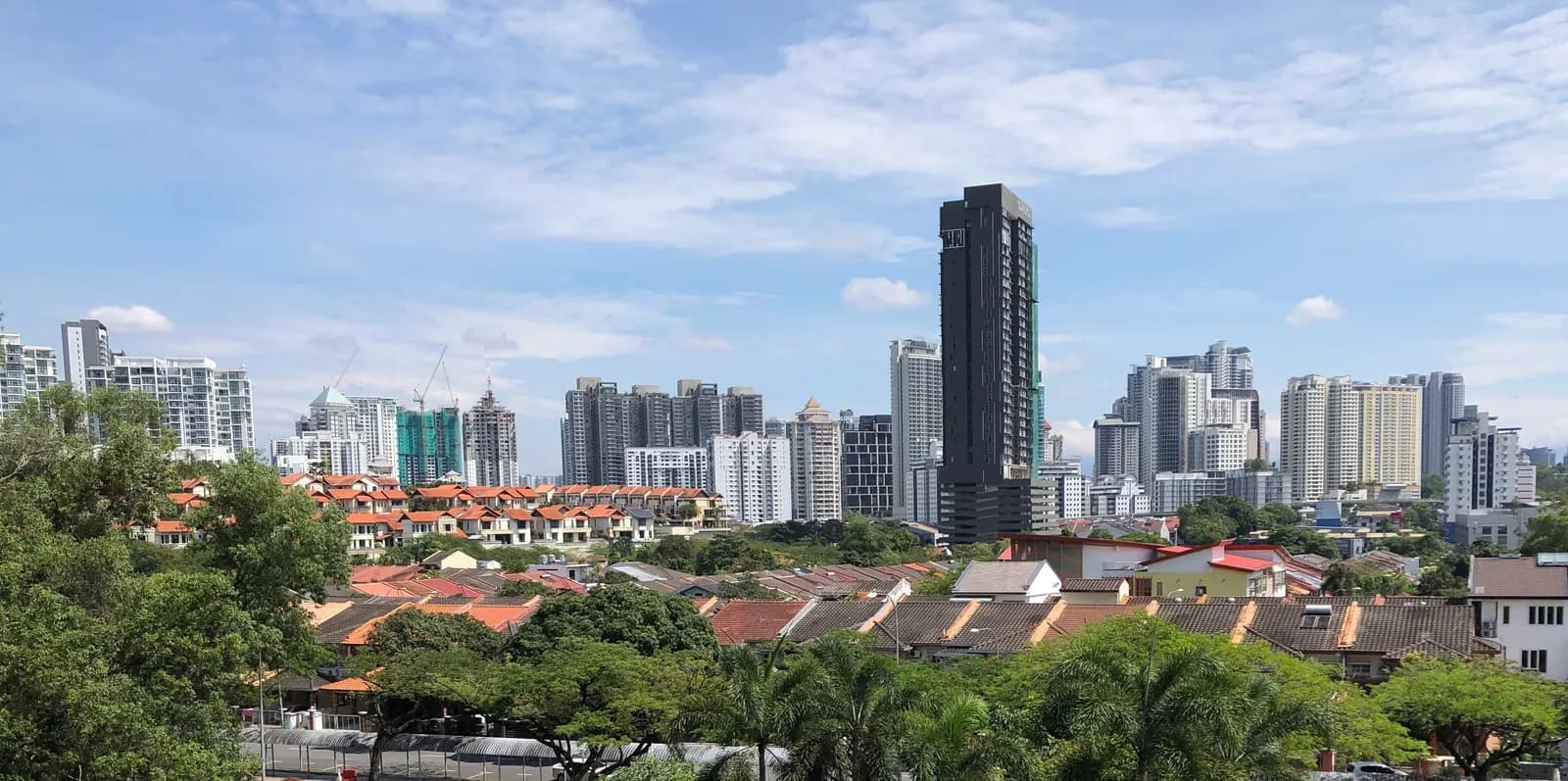 Condominium towers of Mont Kiara rising behind low-rise houses with orange roofs and green trees, under a blue sky