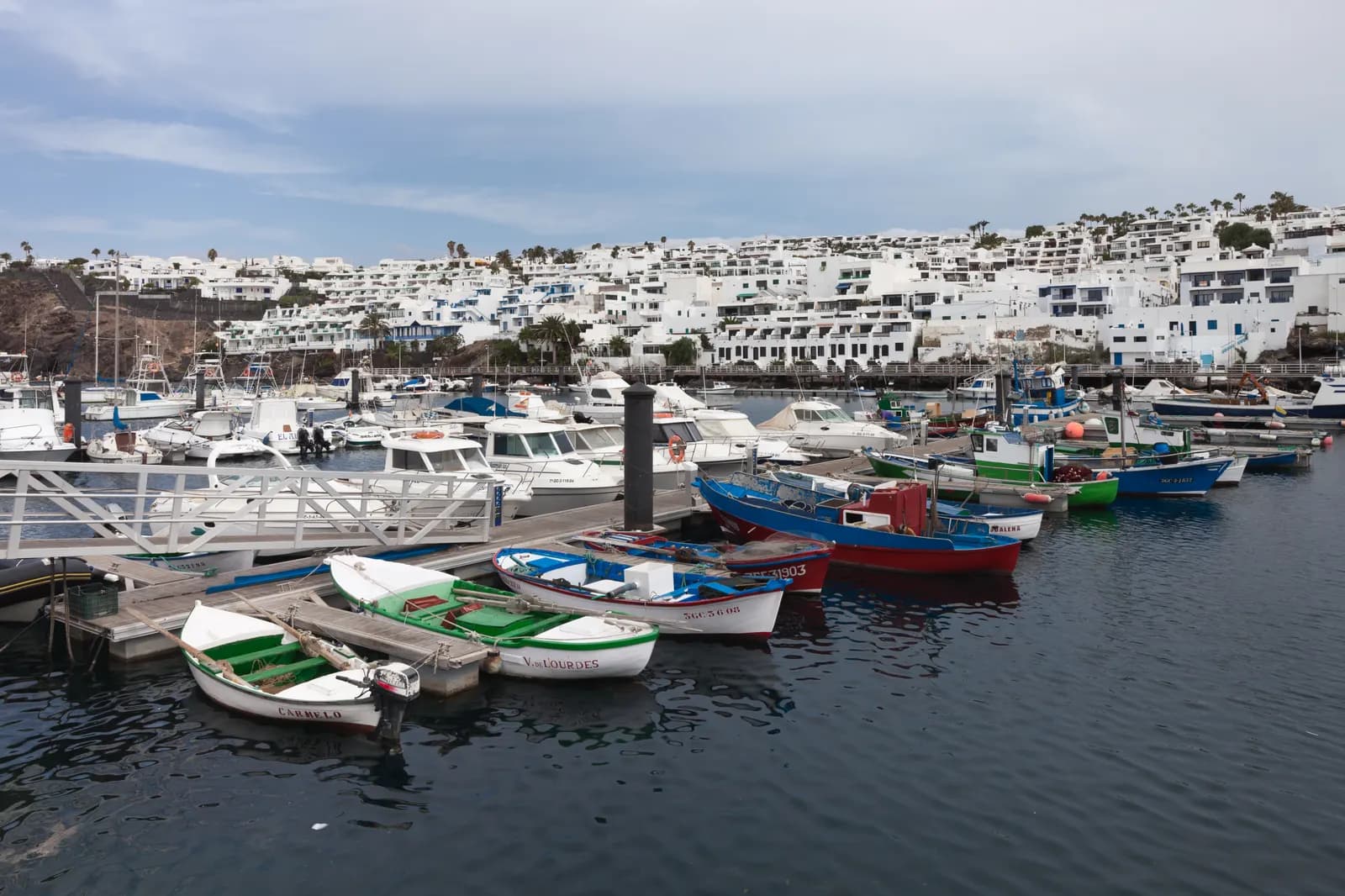 Fishing boats and motorboats in the old harbour of Puerto del Carmen, with white holiday apartments on the slope behind.