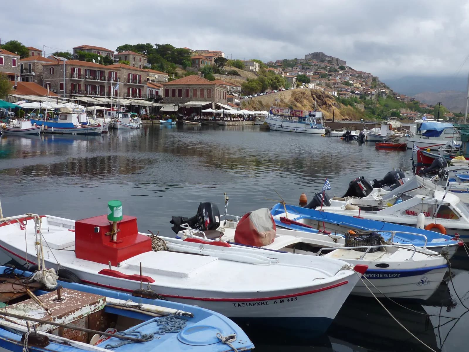 Fishing boats in the small harbour of Molyvos under a cloudy sky, with tavernas on the quay and the castle on the hill