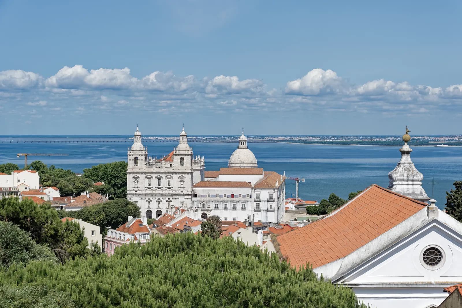 Alfama seen from São Jorge Castle, with the white Monastery of São Vicente de Fora and the dome of the National Pantheon above the river.