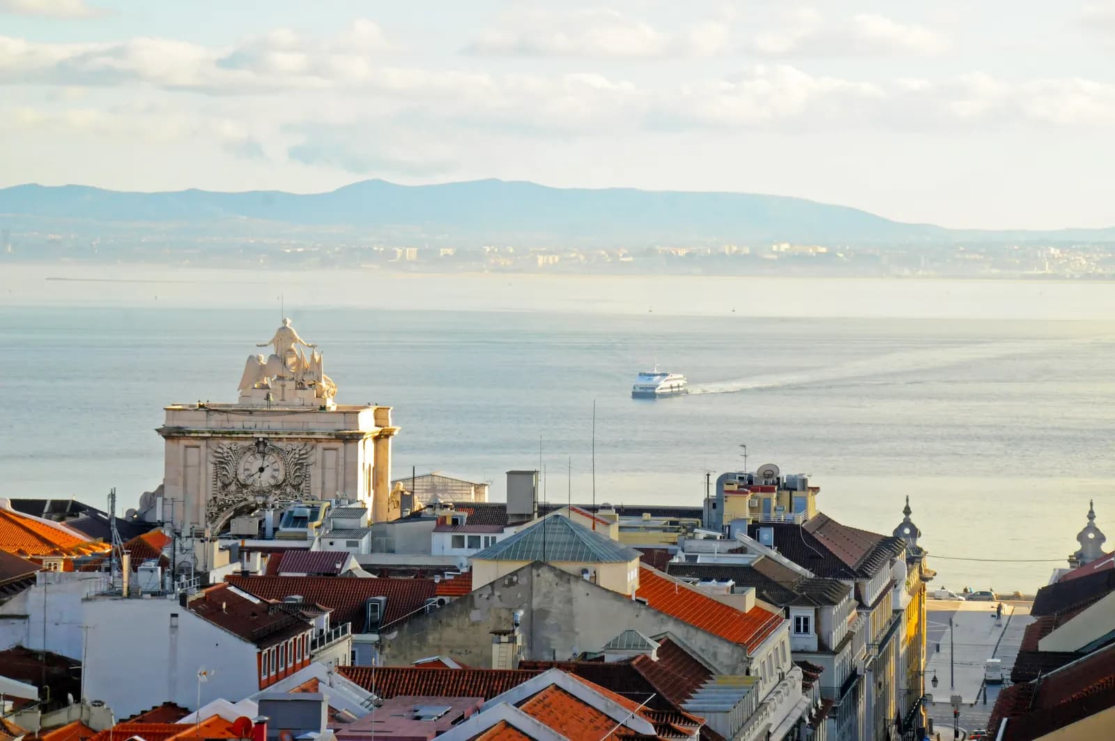 Looking south over the rooftops of the Baixa to the Rua Augusta Arch and the Tagus estuary, with a ferry crossing the river.
