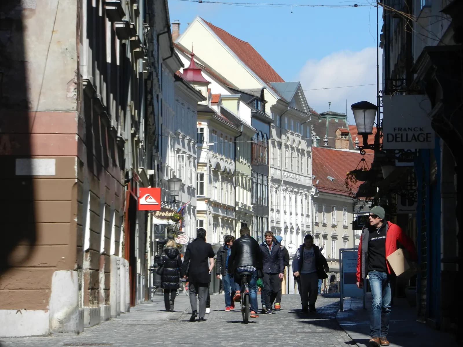 People walking along Mestni trg, the Town Square in Ljubljana old town, between tall pastel houses with lanterns