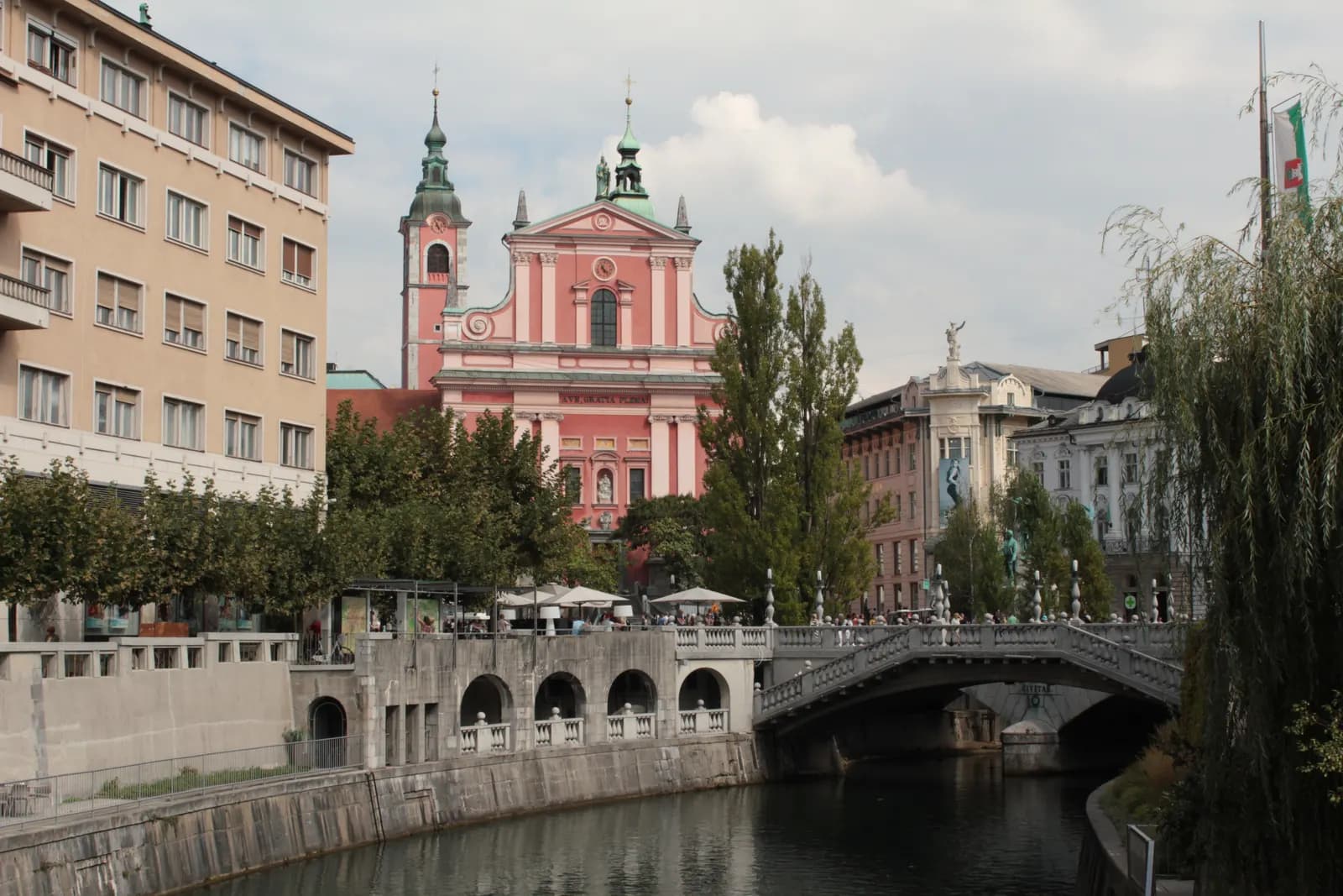 The Triple Bridge over the Ljubljanica with the pink Franciscan Church on Prešeren Square behind, willows and the embankment arcades in front