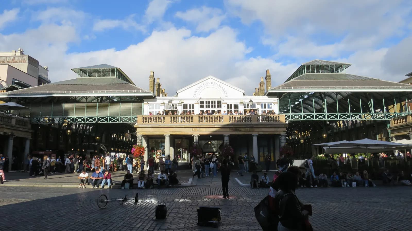 The Covent Garden market building seen across the cobbled piazza, with people sitting and walking in front of it
