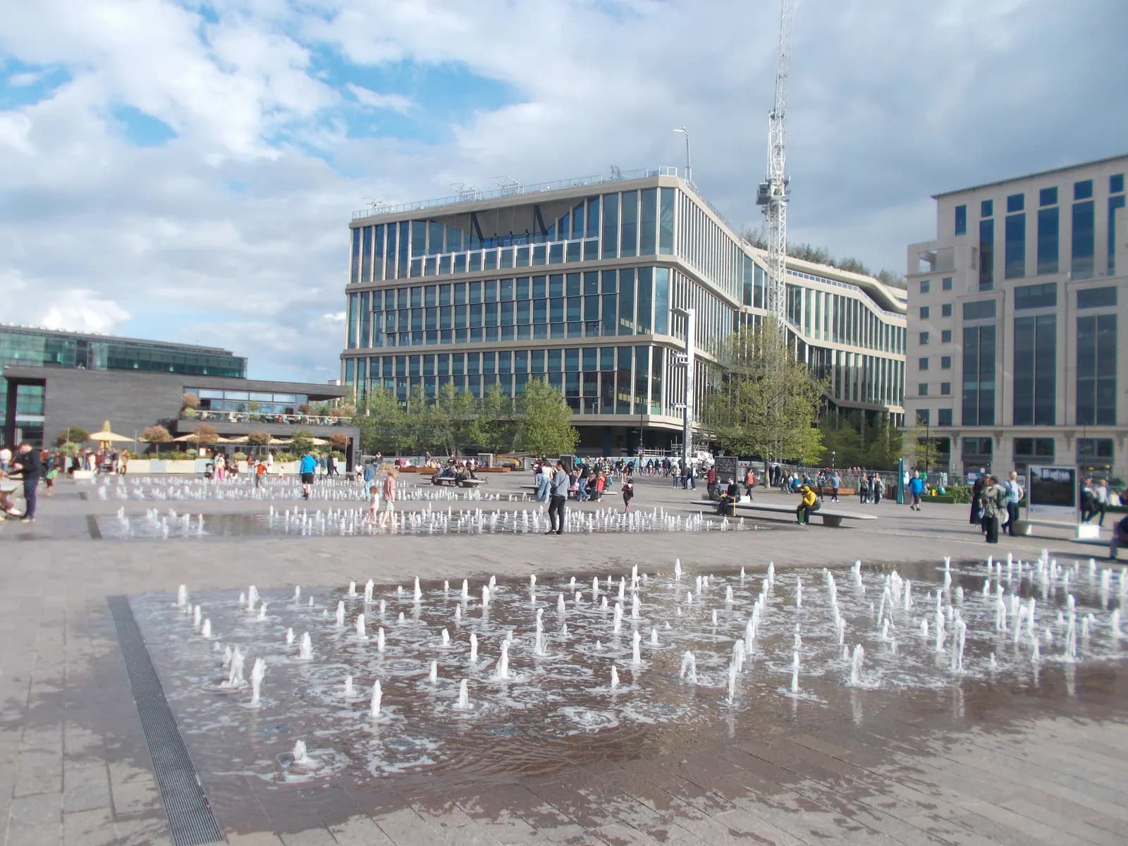 The ground fountains of Granary Square at King's Cross, with office buildings and people walking behind