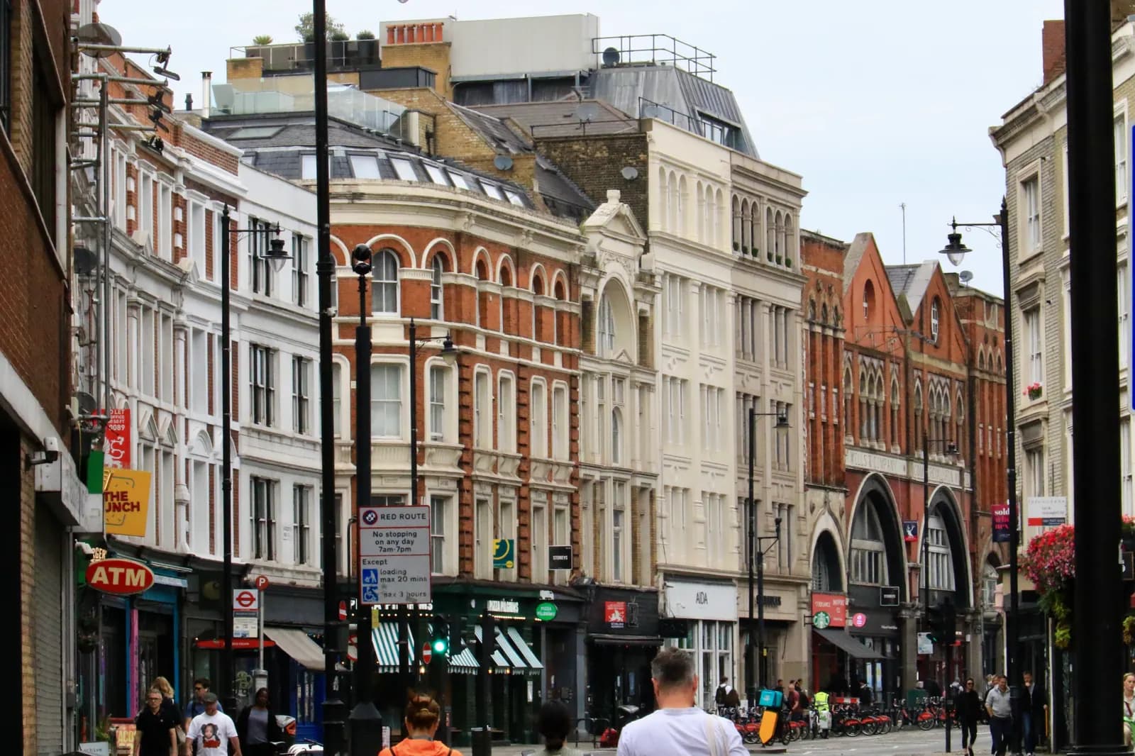 Shoreditch High Street looking north, with Victorian shop buildings, a red route sign and people on the pavement