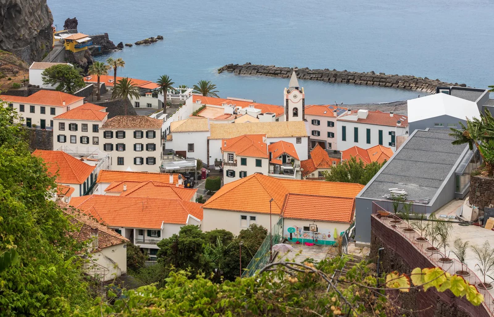 Orange roofs of Ponta do Sol around the white church tower, with the harbour breakwater and the sea behind