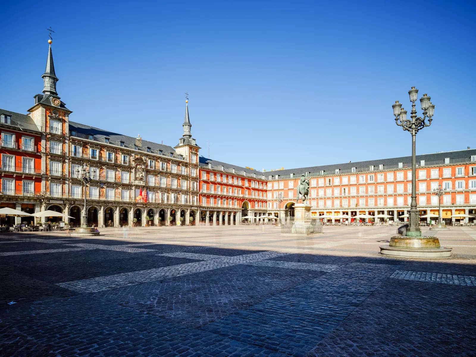 The arcaded Plaza Mayor in Madrid on a clear day, with the painted Casa de la Panadería, the equestrian statue at its centre and a tall street lamp.