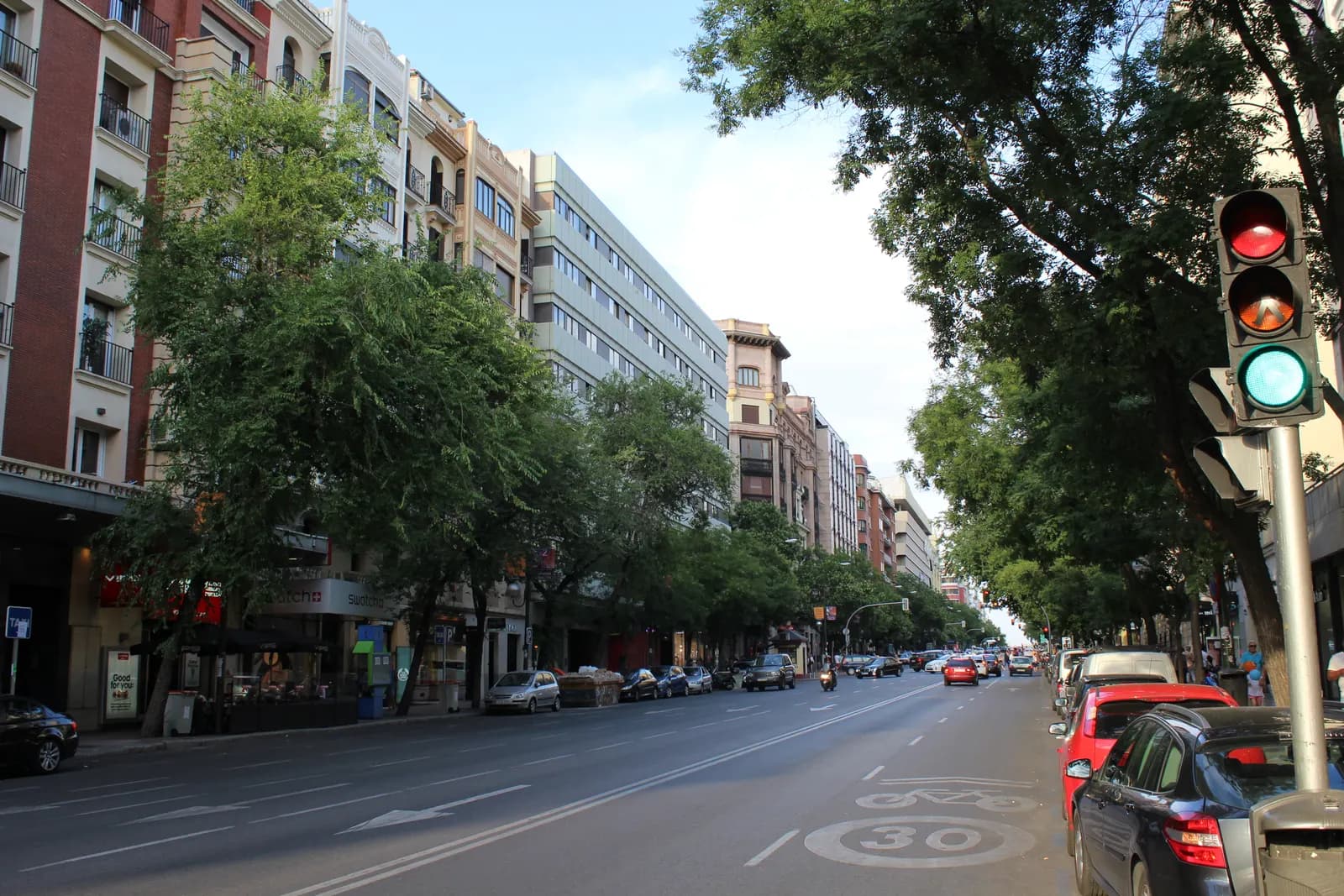 Calle de Goya in the Salamanca district, a wide avenue lined with trees and apartment blocks, with parked cars and a 30 km/h marking on the road.