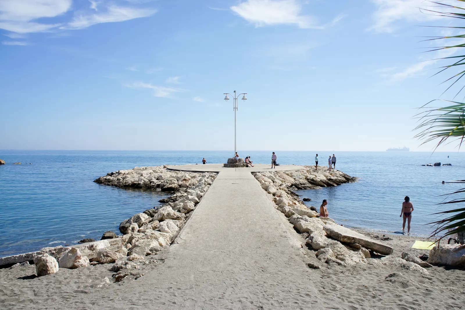 A short stone jetty at Pedregalejo beach reaching into a calm, clear Mediterranean.