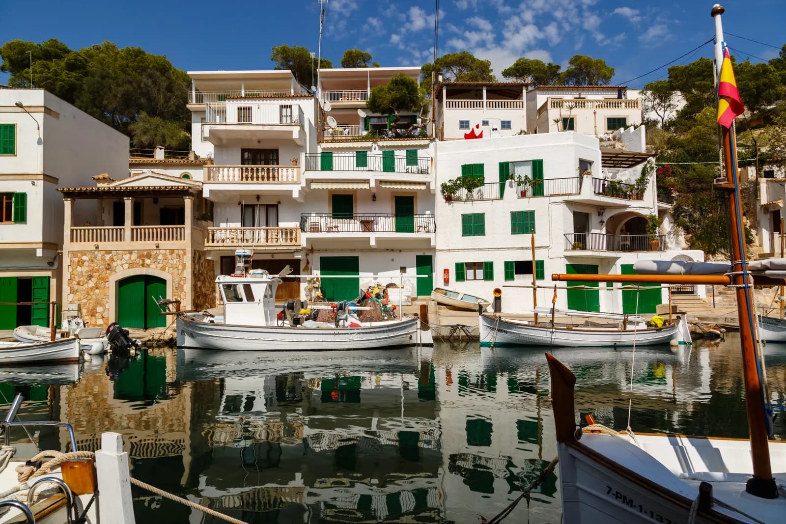 White houses with green shutters above the narrow harbour of Cala Figuera, with fishing boats reflected in the water.