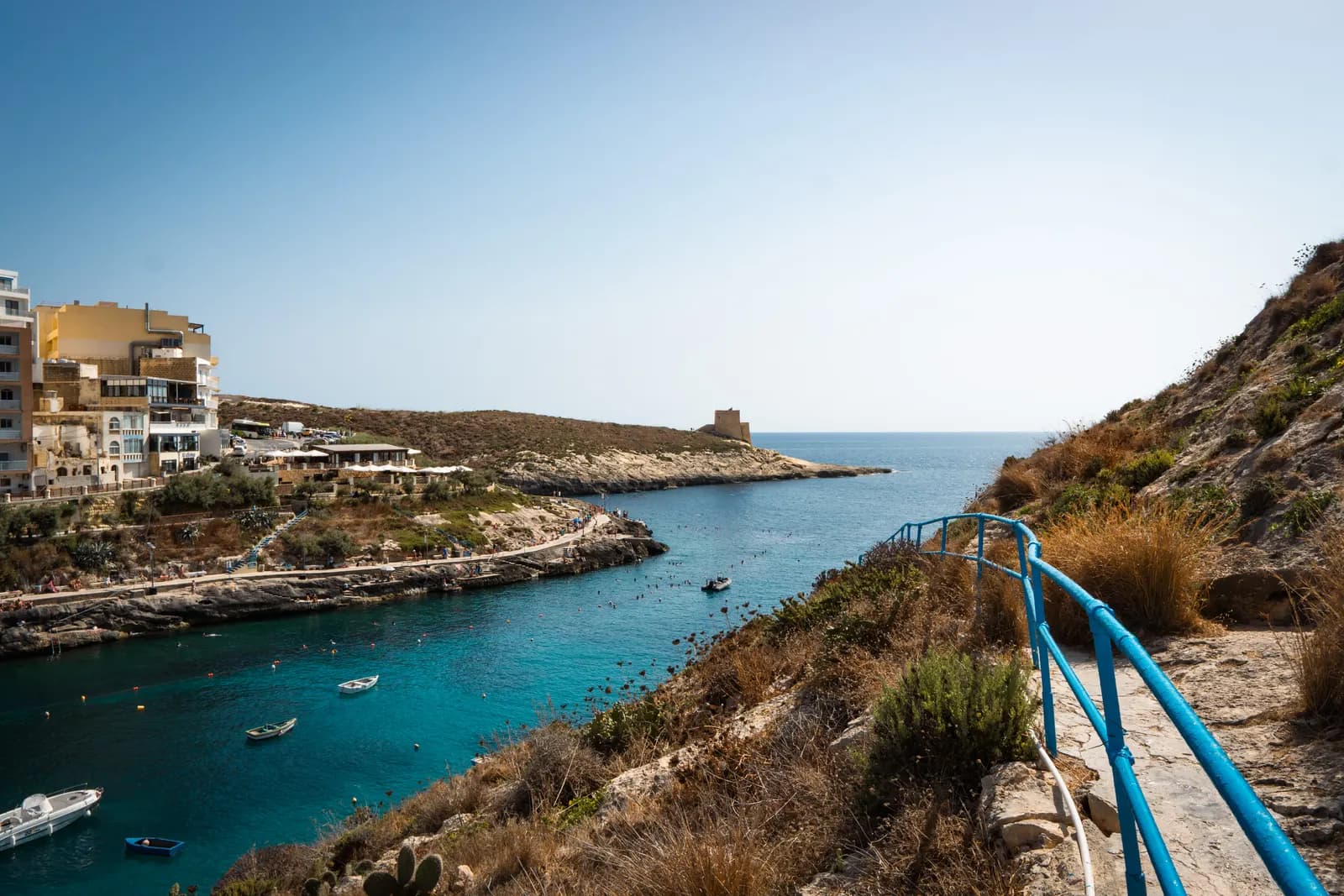 The narrow turquoise inlet of Xlendi Bay on Gozo, with hotels and apartments on the left and the Xlendi watchtower on the headland