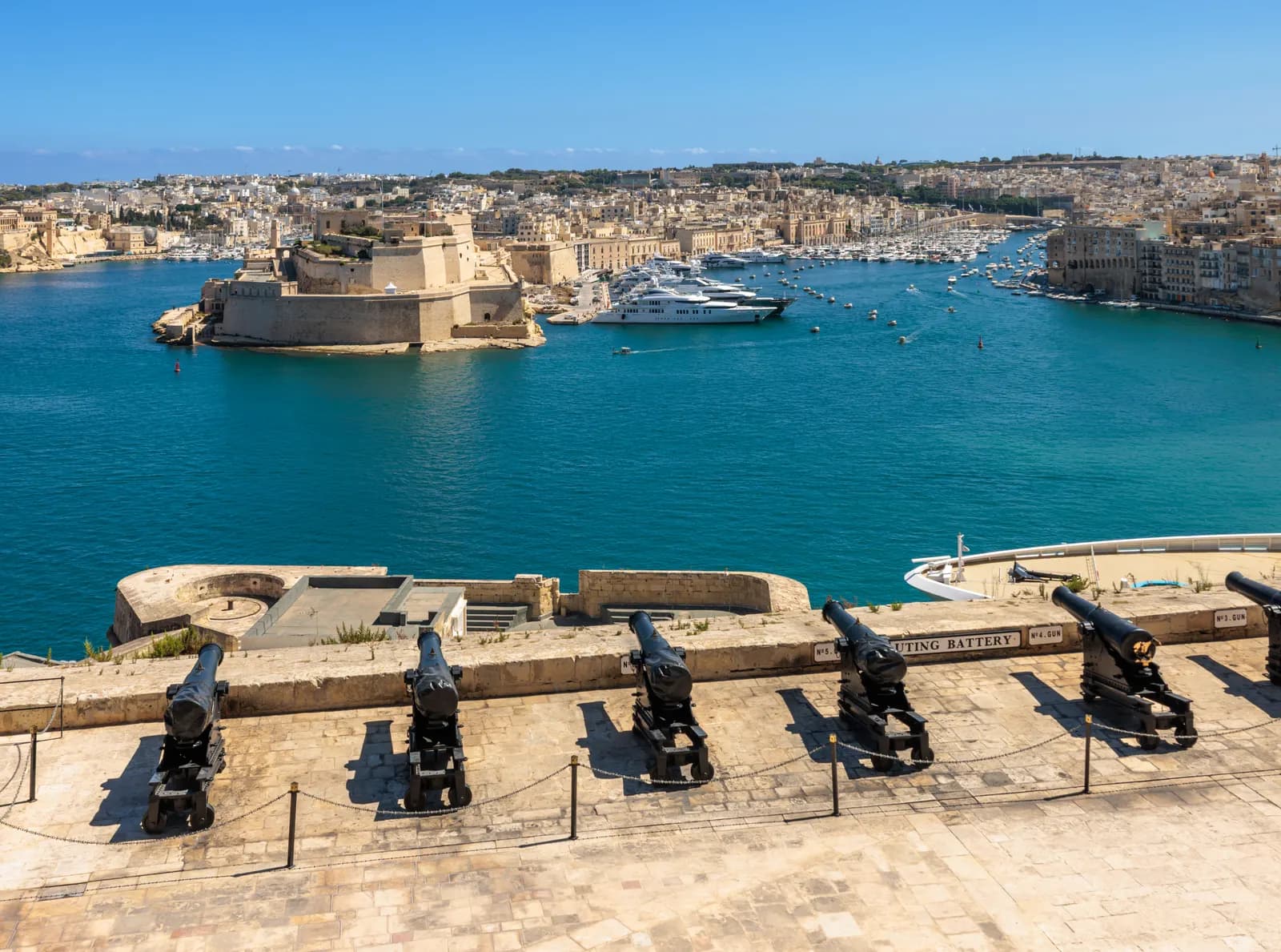 The cannons of the Saluting Battery at the Upper Barrakka Gardens in Valletta, with the Grand Harbour, Fort St Angelo and the Birgu yacht marina beyond