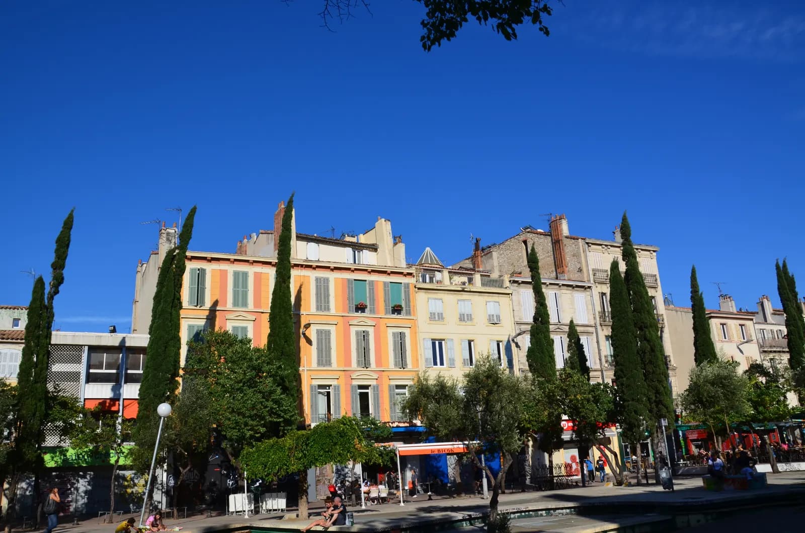 The Cours Julien in Marseille, a long pedestrian square with cypresses and plane trees in front of painted house fronts and street level bars