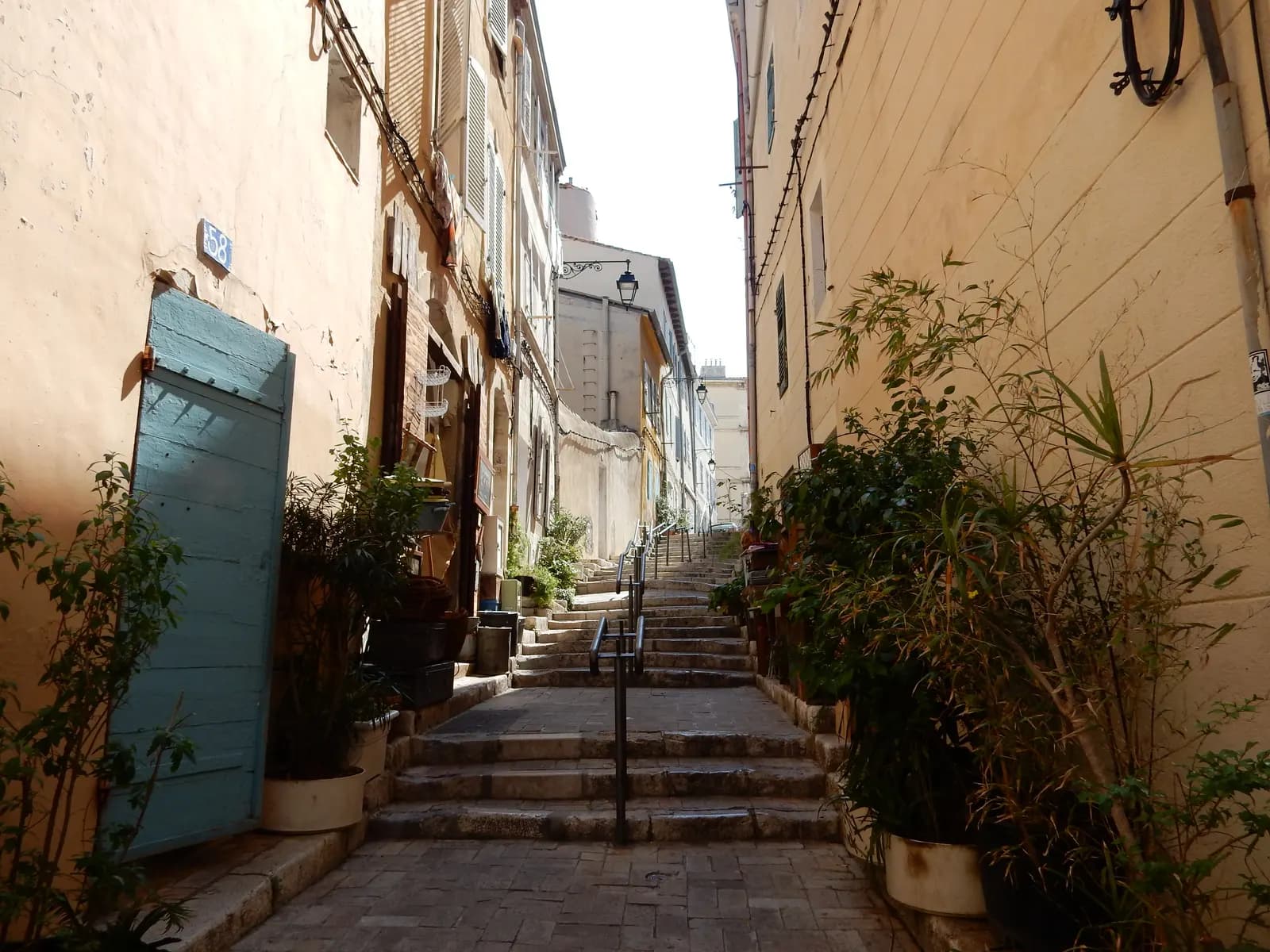 A narrow stepped lane in Le Panier in Marseille, with potted plants, shutters and lanterns along the house fronts and no room for a car