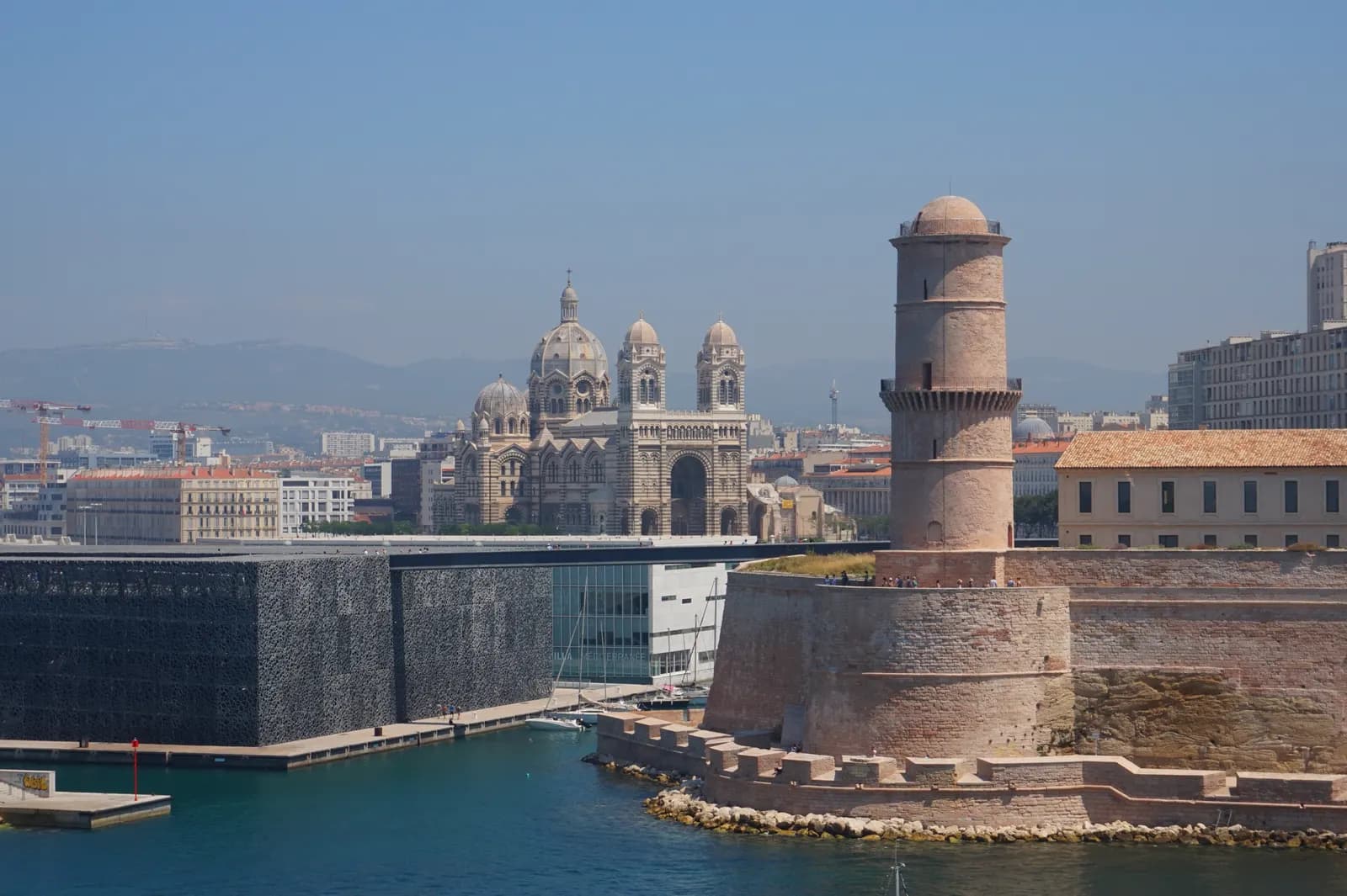 The dark latticework of the MuCEM museum and the tower of Fort Saint-Jean at the entrance to the Vieux-Port, with the striped Marseille cathedral behind