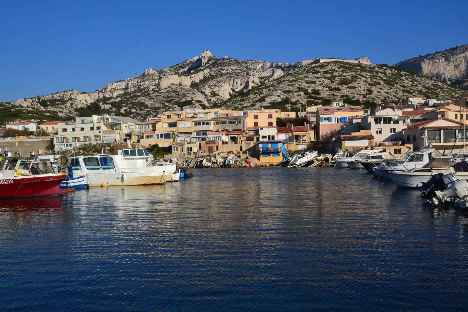 The small harbour of Les Goudes at the southern end of Marseille, with fishing boats, low white houses and the bare limestone ridge of the Calanques behind