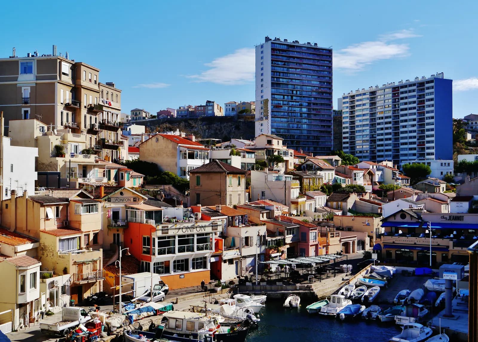 The fishing harbour of the Vallon des Auffes below the Corniche in Marseille, with small boats, quayside restaurants and tower blocks on the cliff above