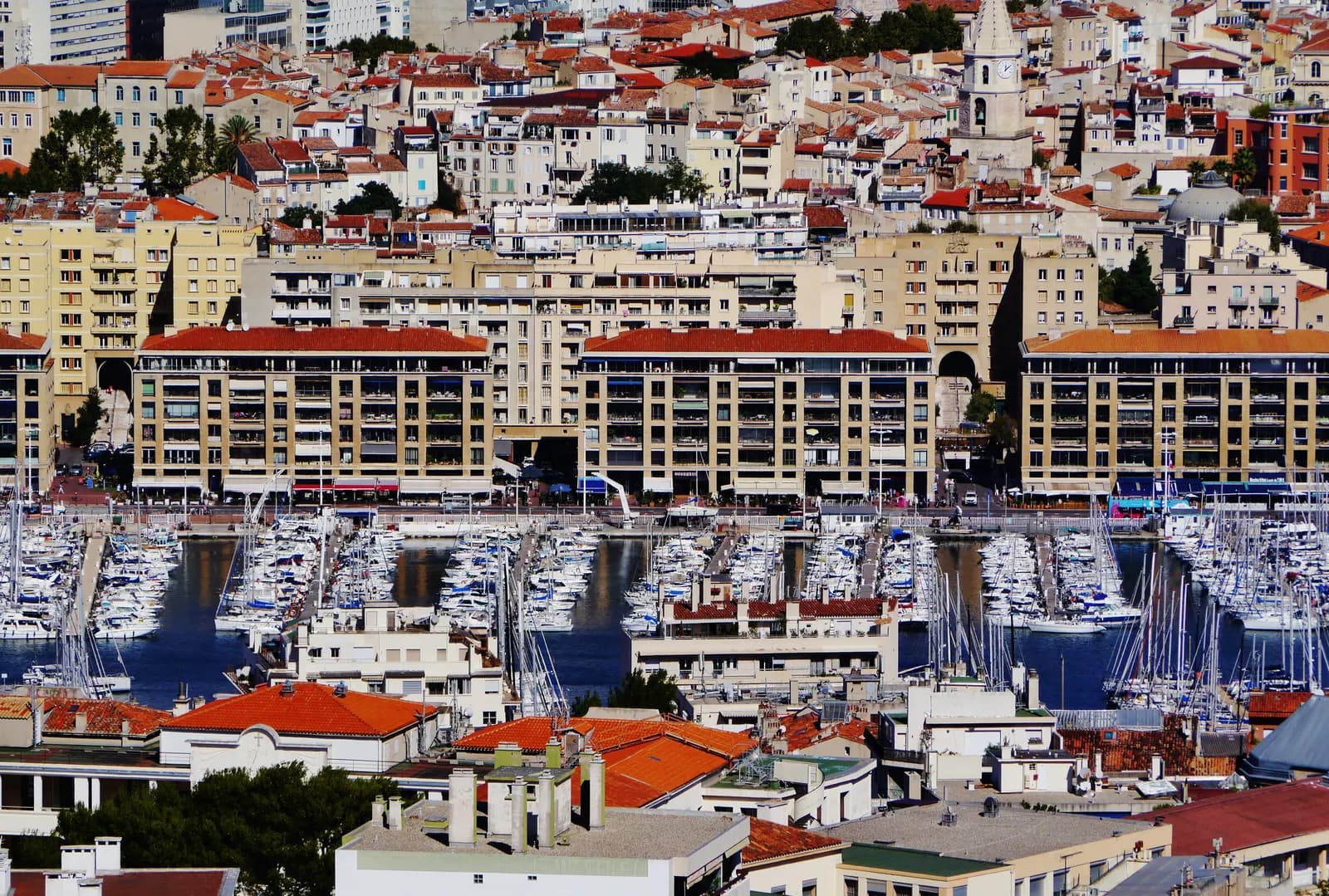 The Vieux-Port of Marseille packed with moored yachts, seen from the hill of Notre-Dame-de-la-Garde over the roofs of the old town