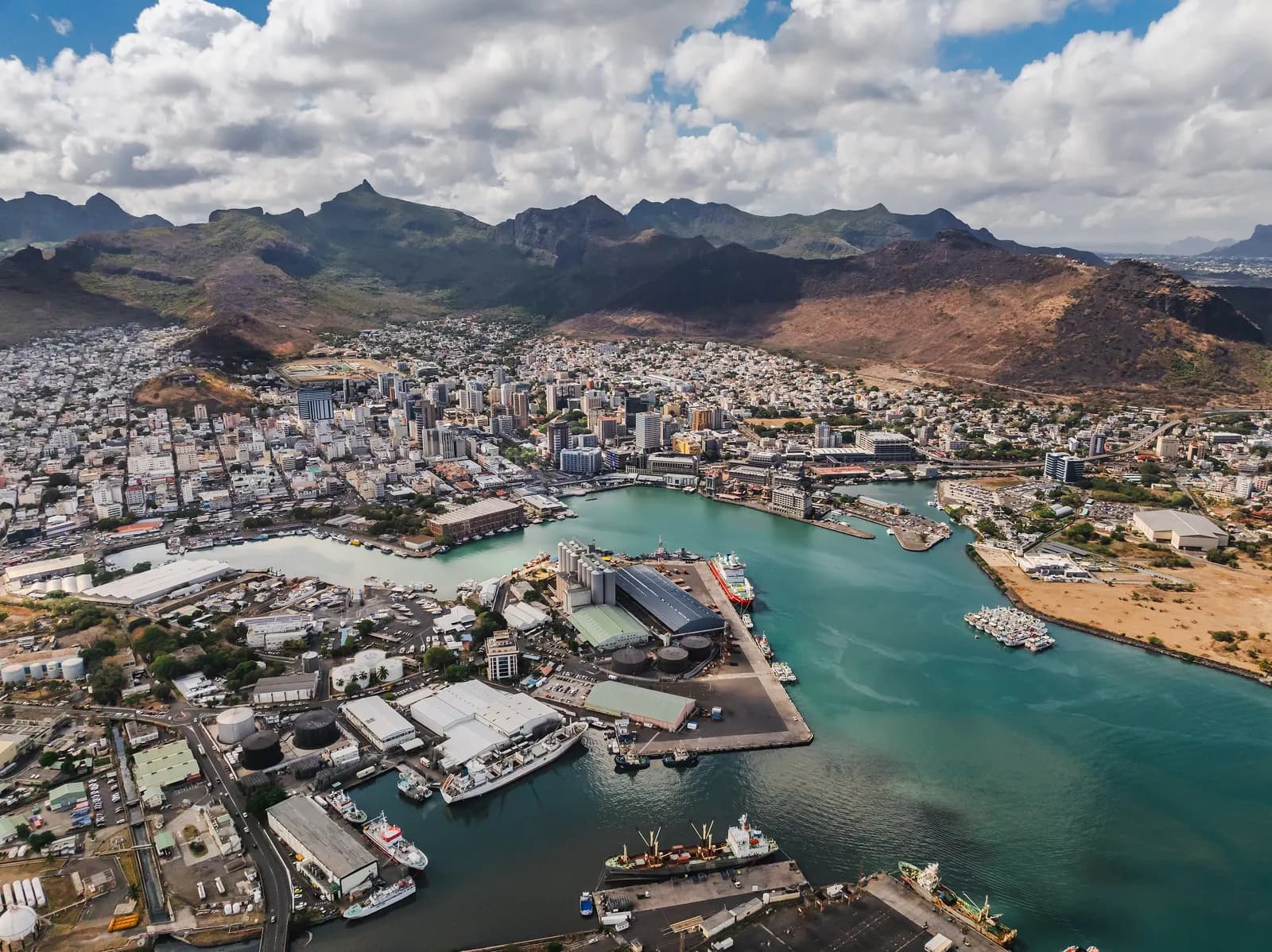 Aerial view of Port Louis, with the harbour, its quays and ships in front, the city's towers and houses behind and mountains under a cloudy sky