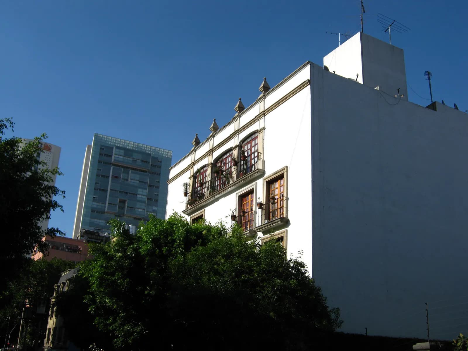 A white three-storey building with arched windows, iron balconies and potted plants on Calle Havre in Colonia Juárez, with a glass office tower behind it under a blue sky