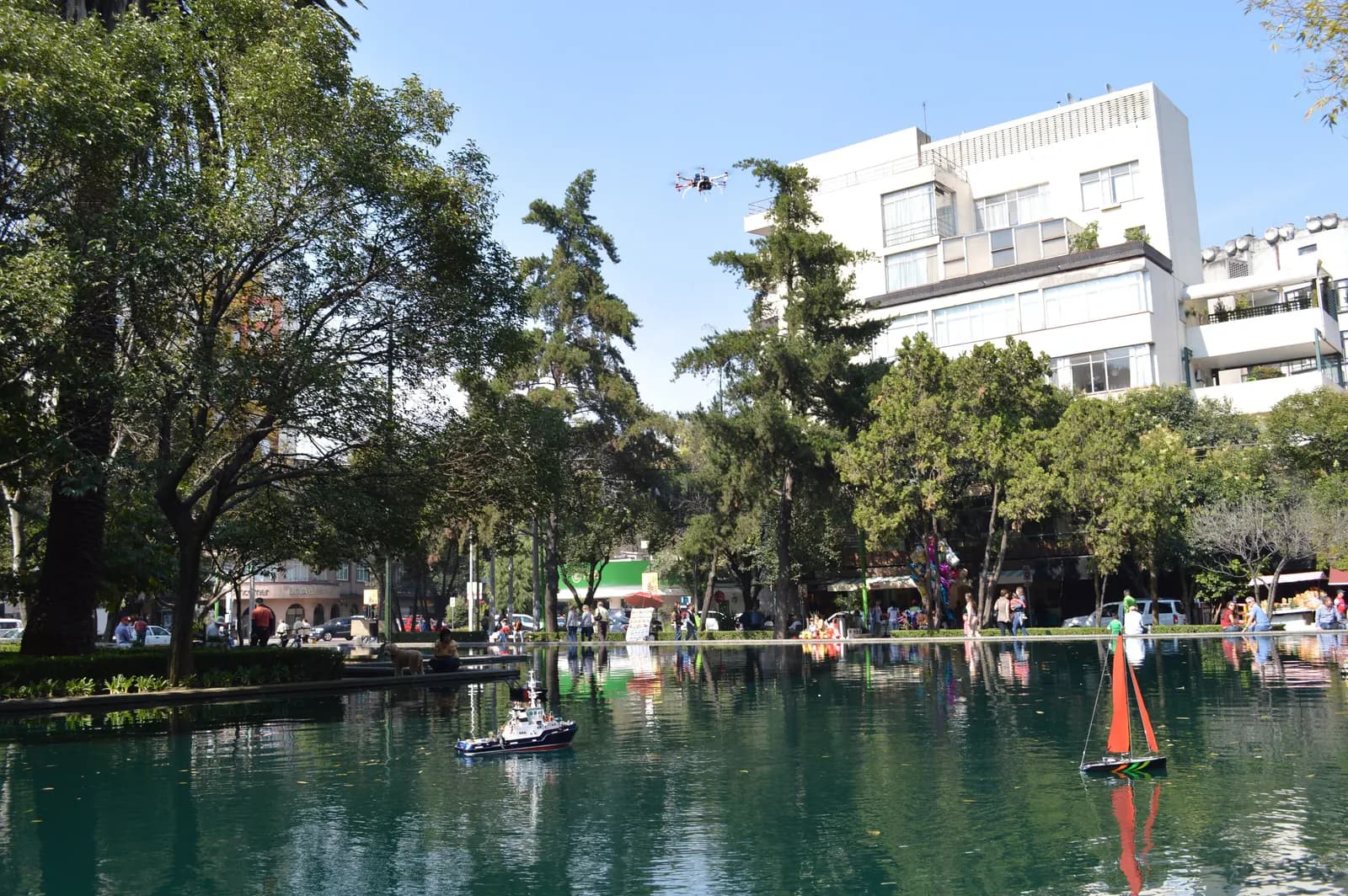 The pond in Lincoln Park in Polanco, with model boats on the water, trees along the edge and white apartment buildings behind under a blue sky